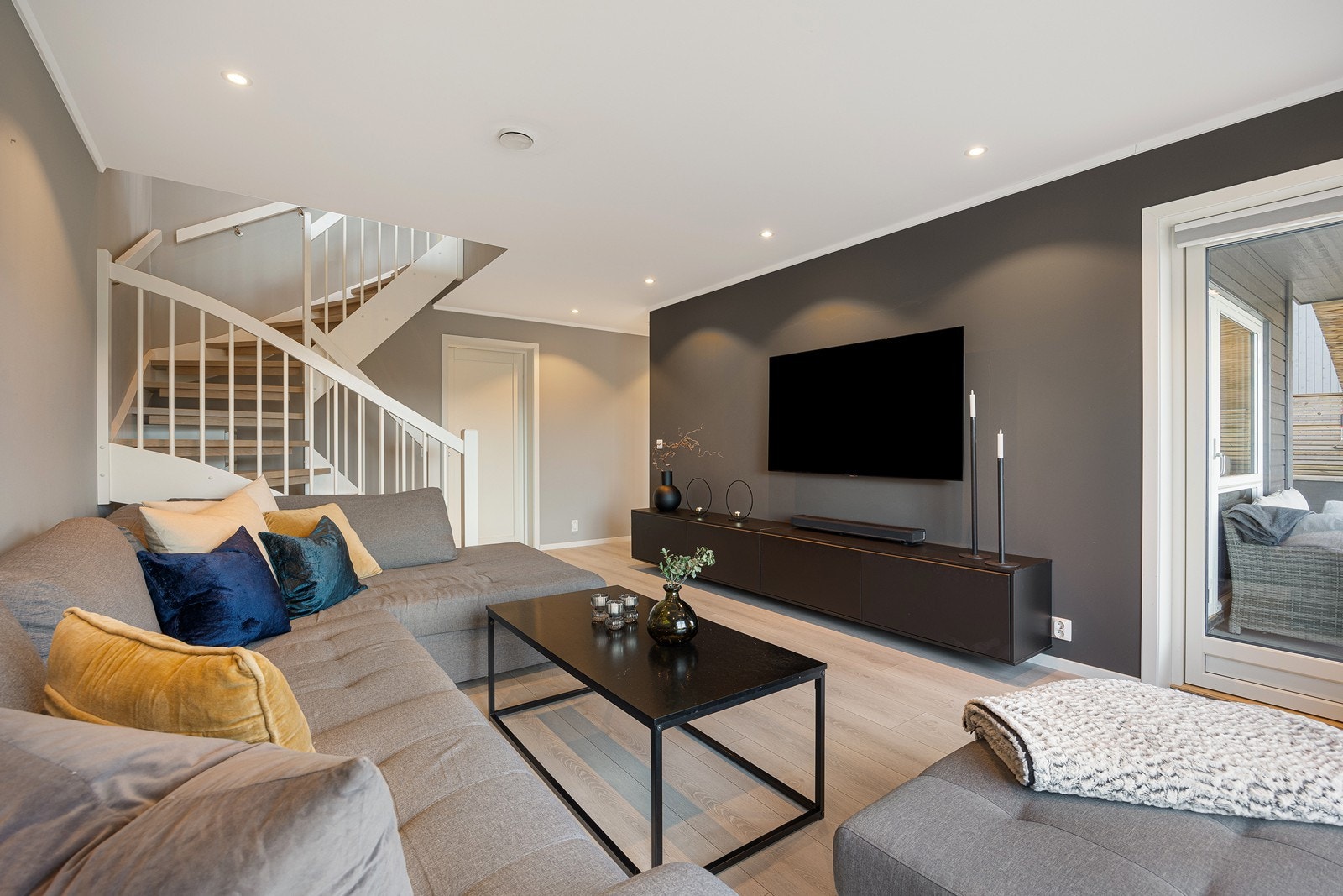 Stuen i underetasjen har samme stil som hovedetasjen med 1-stavs laminat, downlights og vegger i ulike gråfarger. En glassdør fører ut til den store markterrassen med utekjøkken. Galleribilde