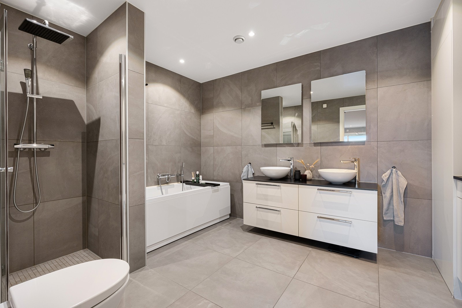 Det lekre badet har varme i gulvet, downlights og vegghengt toalett. Plassert under to speil har badet en hvit skuffeseksjon med to toppmonterte servantskåler. Galleribilde