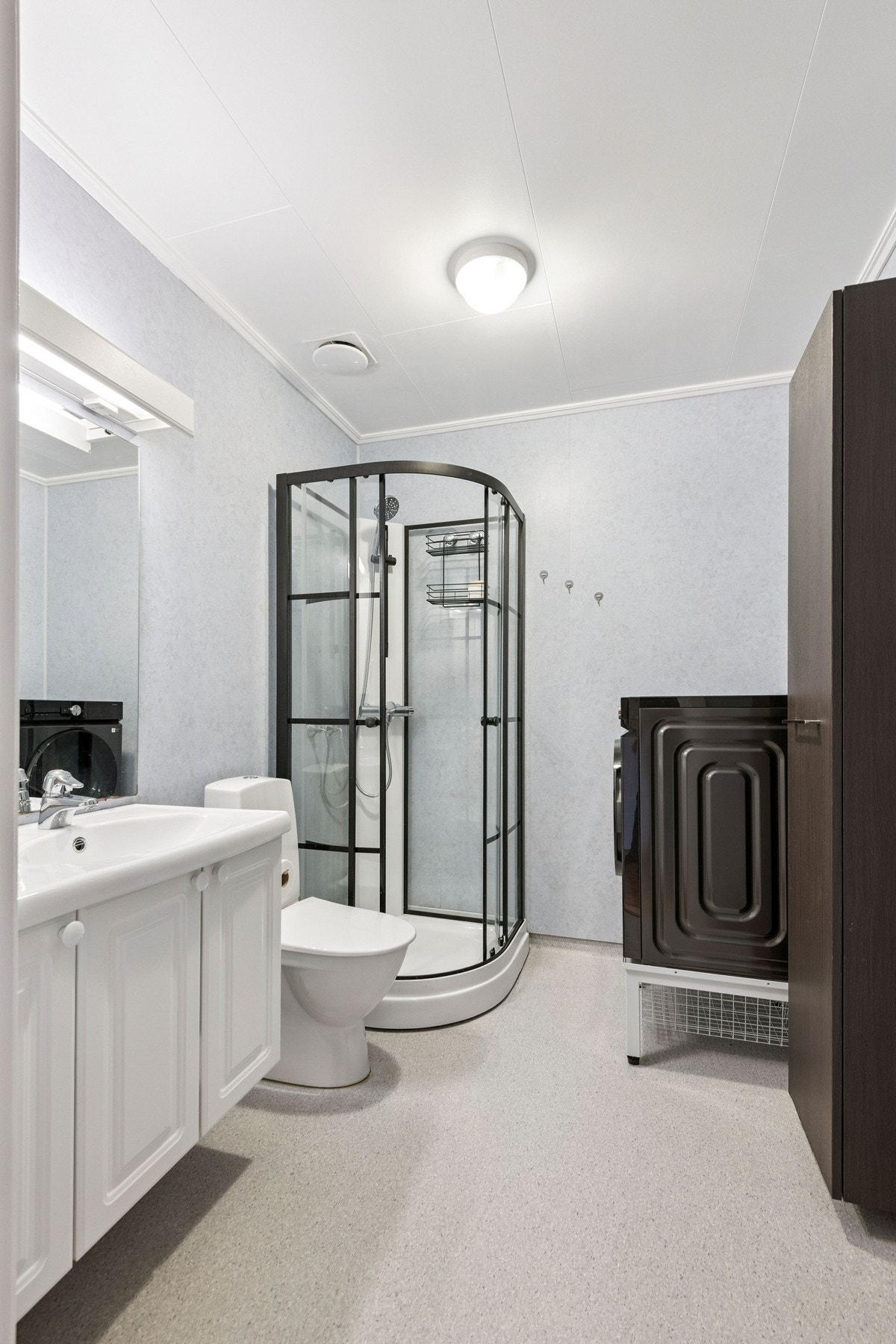 Lyst bad innredet med servant, dusjkabinett, gulvmontert toalett, høyskap og opplegg for vaskemaskin. Galleribilde