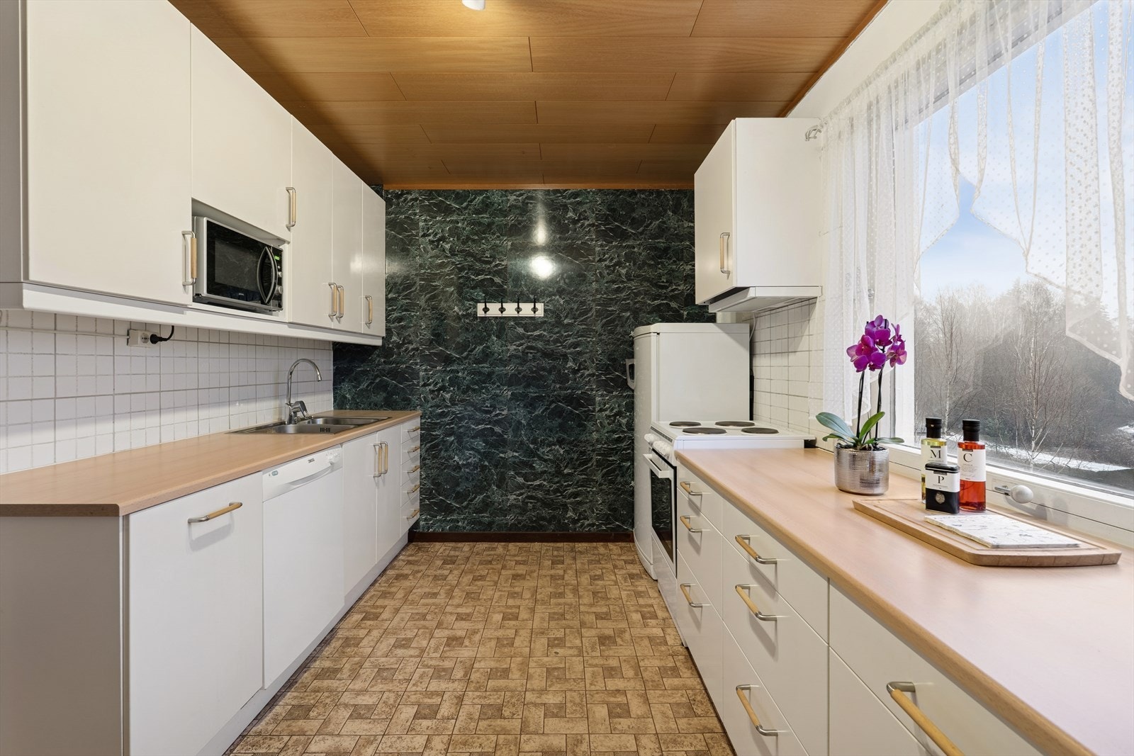 Kjøkkenet ligger adskilt fra stuen. Eldre hvit innredning med slette fronter og benkeplate av laminat. Hvitevarer medfølger i handelen, se pkt. hvitevarer Galleribilde