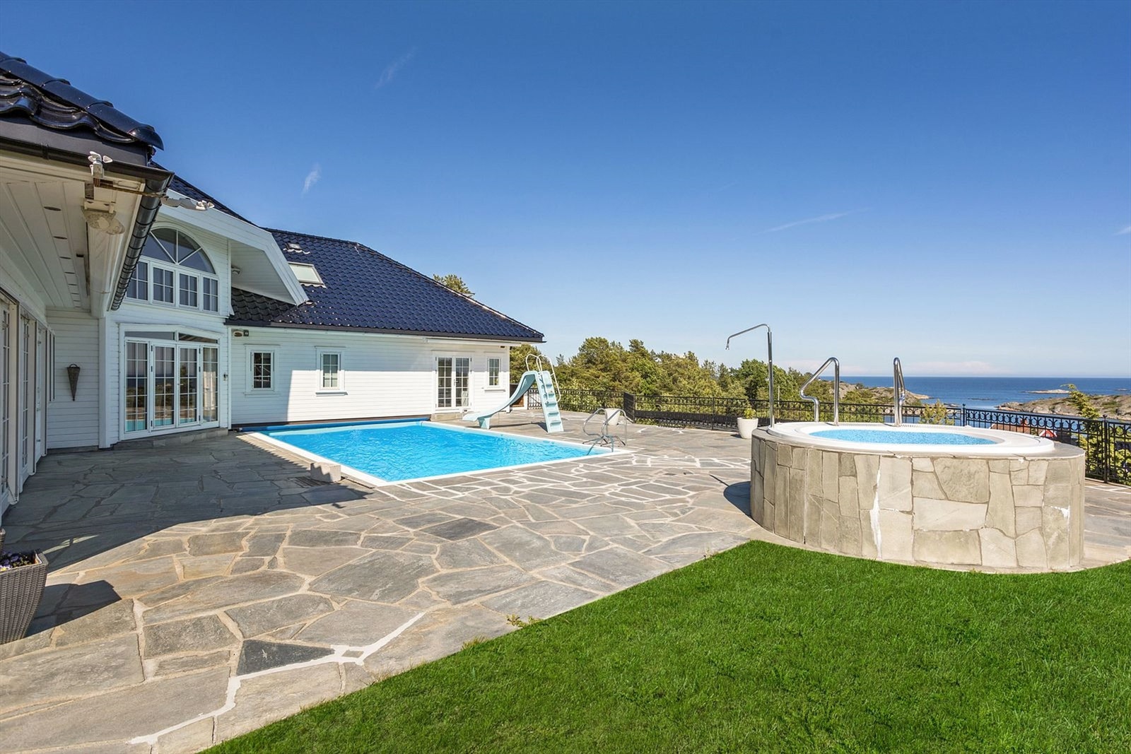 Fantastisk uteplass med fritt utsyn, basseng som har motstrømspumpe, boblebad, skiferbelagt uteplass, smijernsgjerde, utebelysning og beplantninger for å nevne noe av hva eiendommen byr på Galleribilde