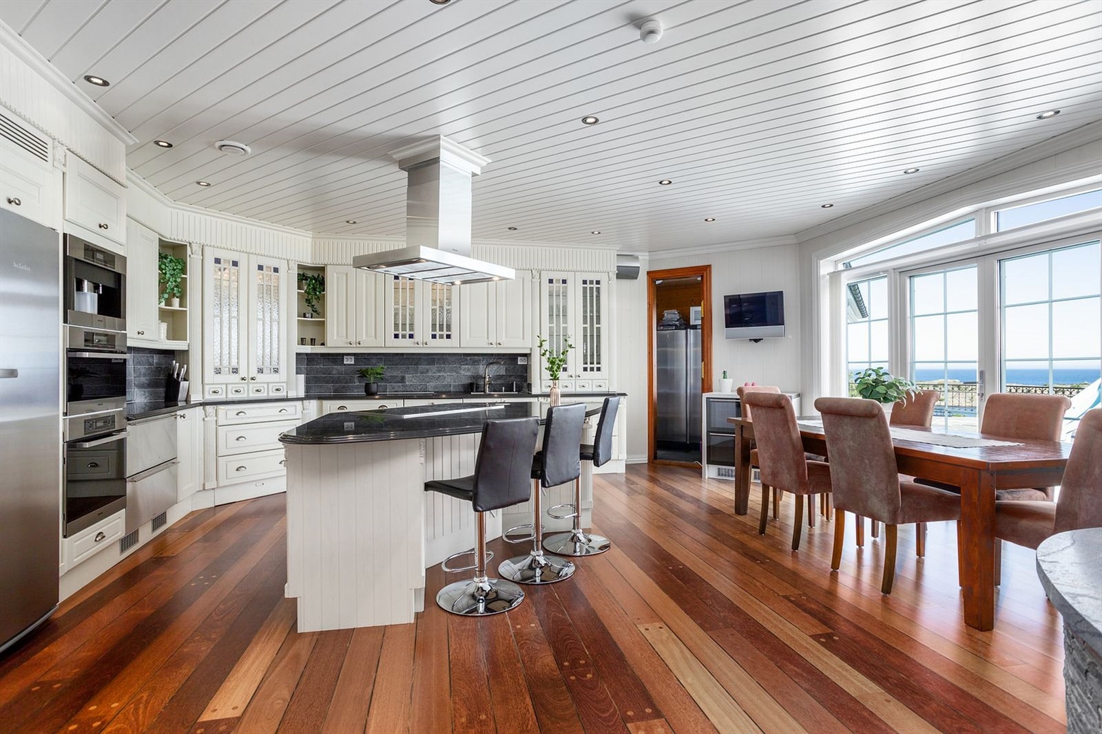 Svært innholdsrikt kjøkken i hovedplan med steinplate, kjøkkenøy og integrerte Miele hvitevarer. Matbod på innsiden av kjøkkenet Galleribilde