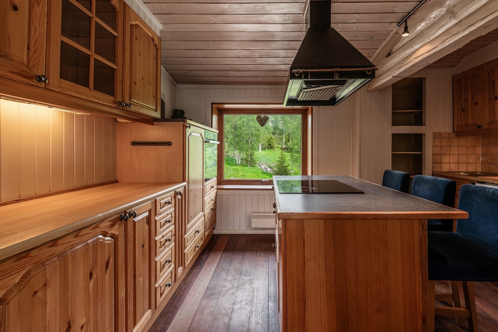 Kjøkkeninnredningen med fronter av heltre som er profilerte. Benkeplaten i laminat og integrert komfyr i høyskap Galleribilde