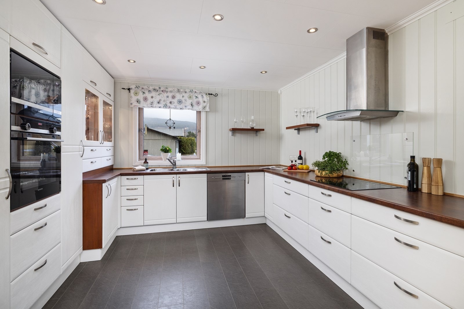 Flott innholdsrikt kjøkken med integrerte hvitevarer, lange arbeidsbenker og downlights i himling. Galleribilde