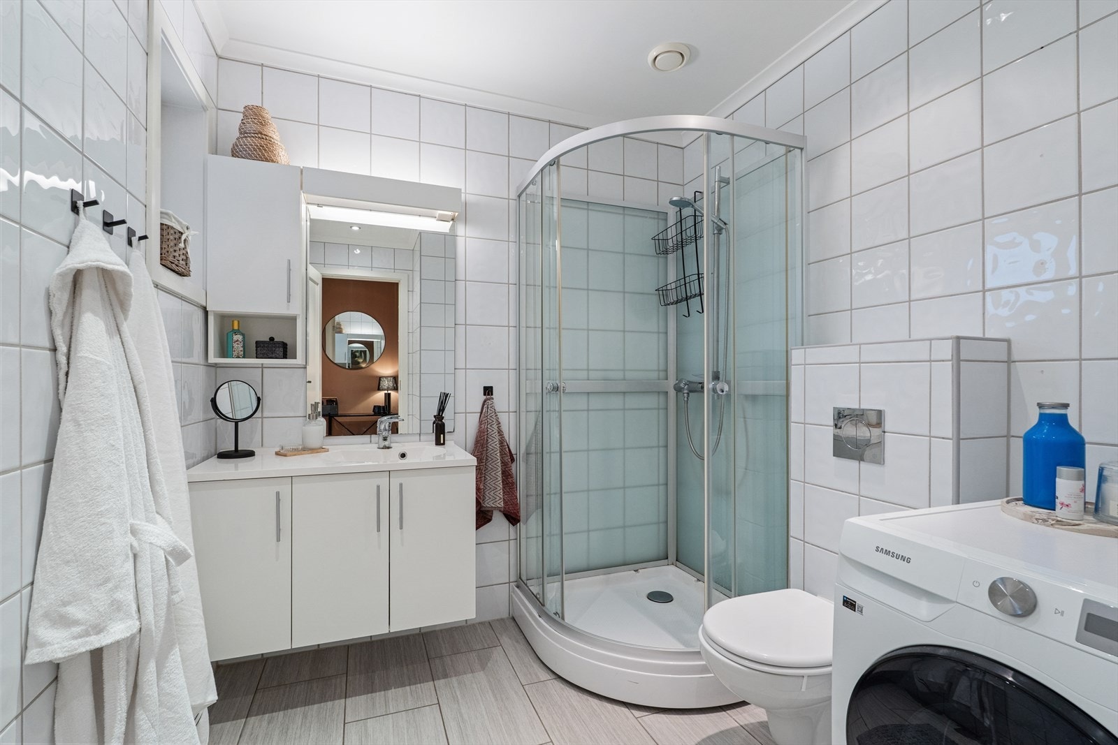 Delikat flislagt bad med behagelig gulvvarme. Badet er utstyrt med dusjkabinett, vegghengt toalett, lys baderomsinnredning og opplegg for vaskemaskin. Galleribilde