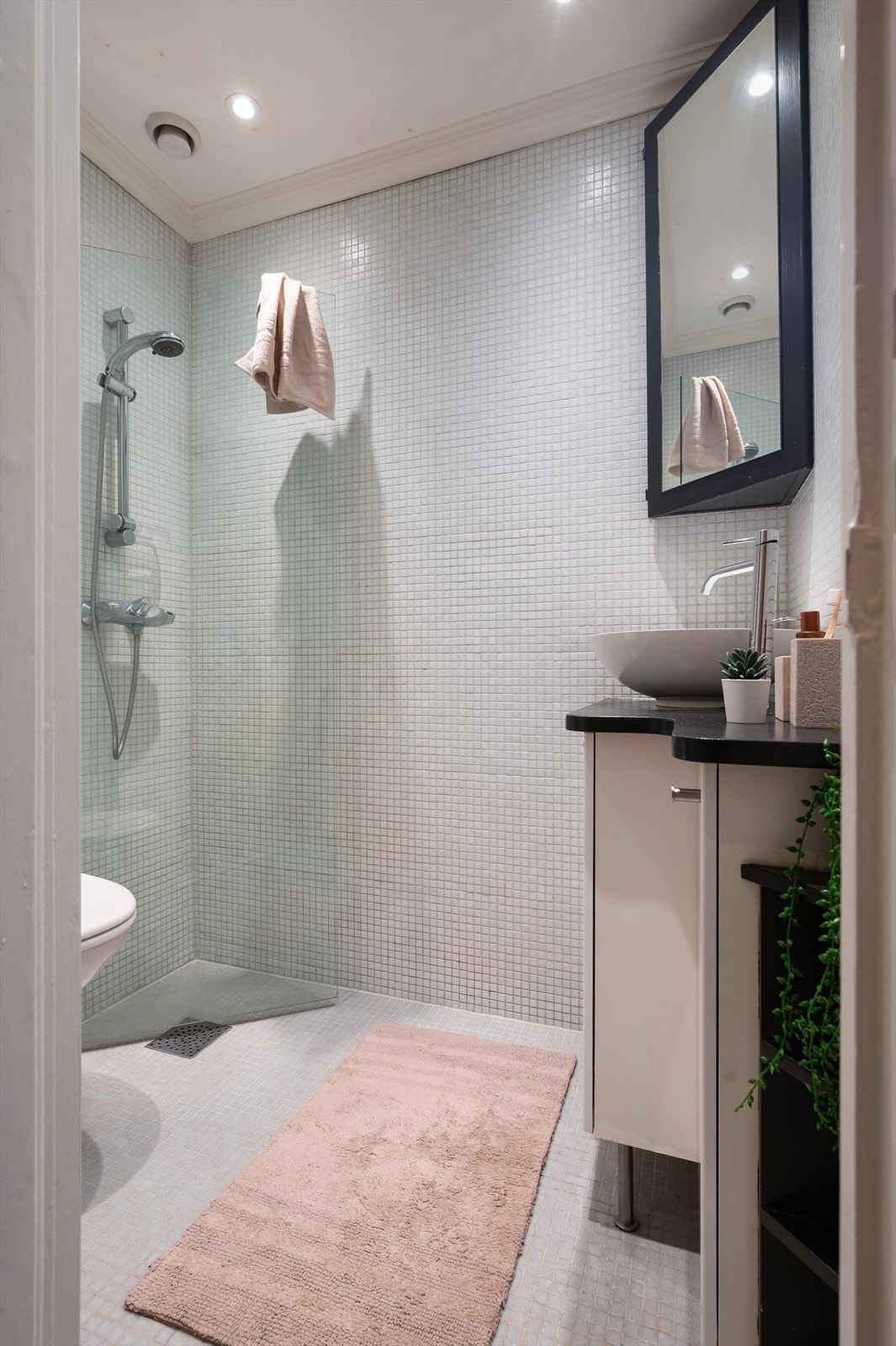 Badet har dusj på gulv med innfellbar dusjvegg, servant med skapinnredning og klosett med vegghengt klosettskål Galleribilde