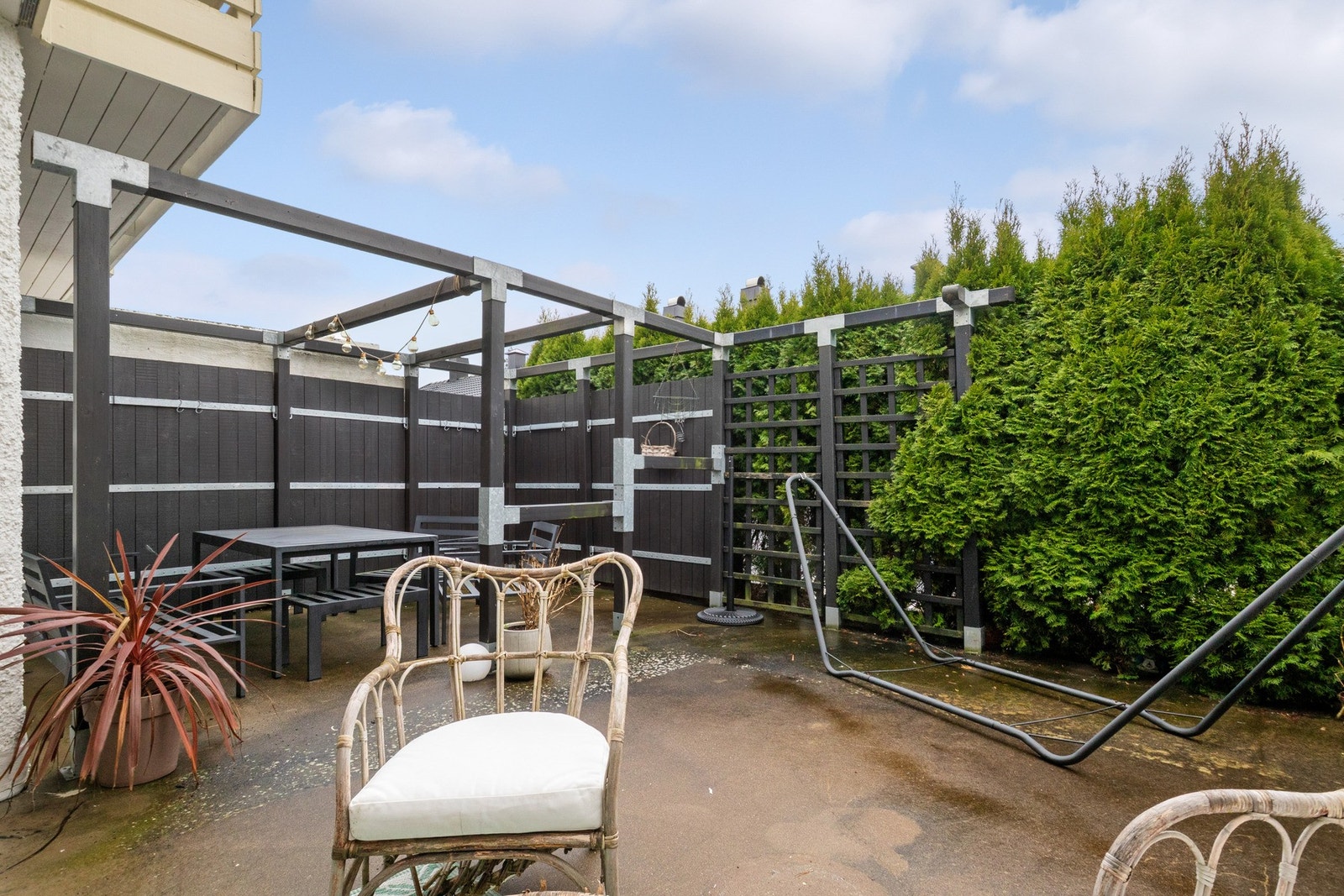 Vestvendt terrasse som oppleves skjermet, med pergola, levegger og høy hekk i front. Galleribilde