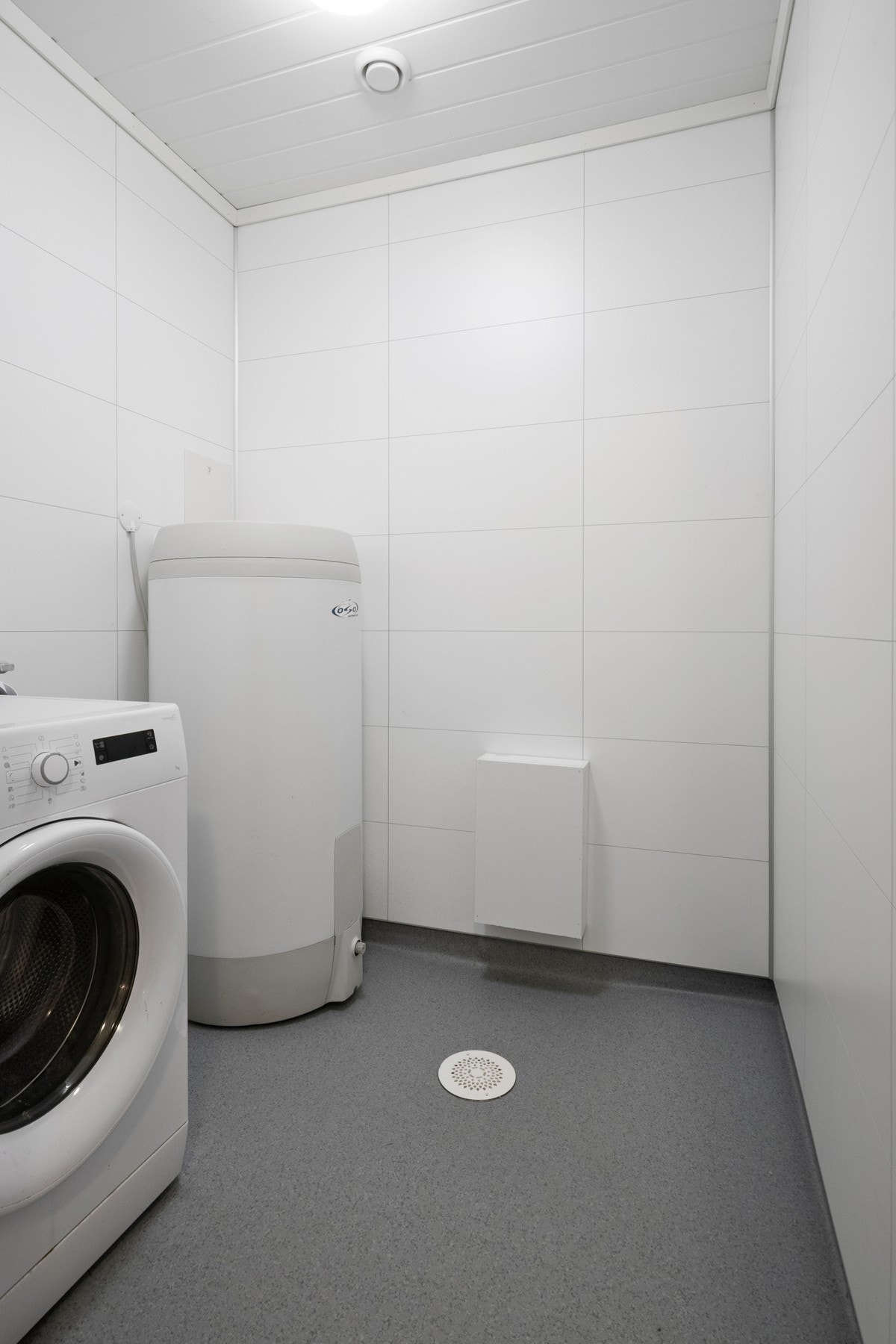 Praktisk vaskerom med opplegg for vaskemaskin, våtromsbelegg på gulv og plass til varmtvannstank. Galleribilde