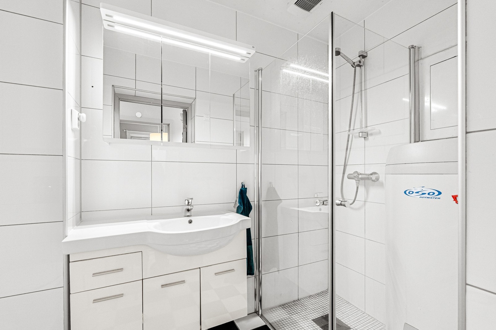 Baderommet inneholder dusj, veggmontert WC, rørskap, varmtvannsbereder, servantplate på underskap, overskap og speilskap. Galleribilde