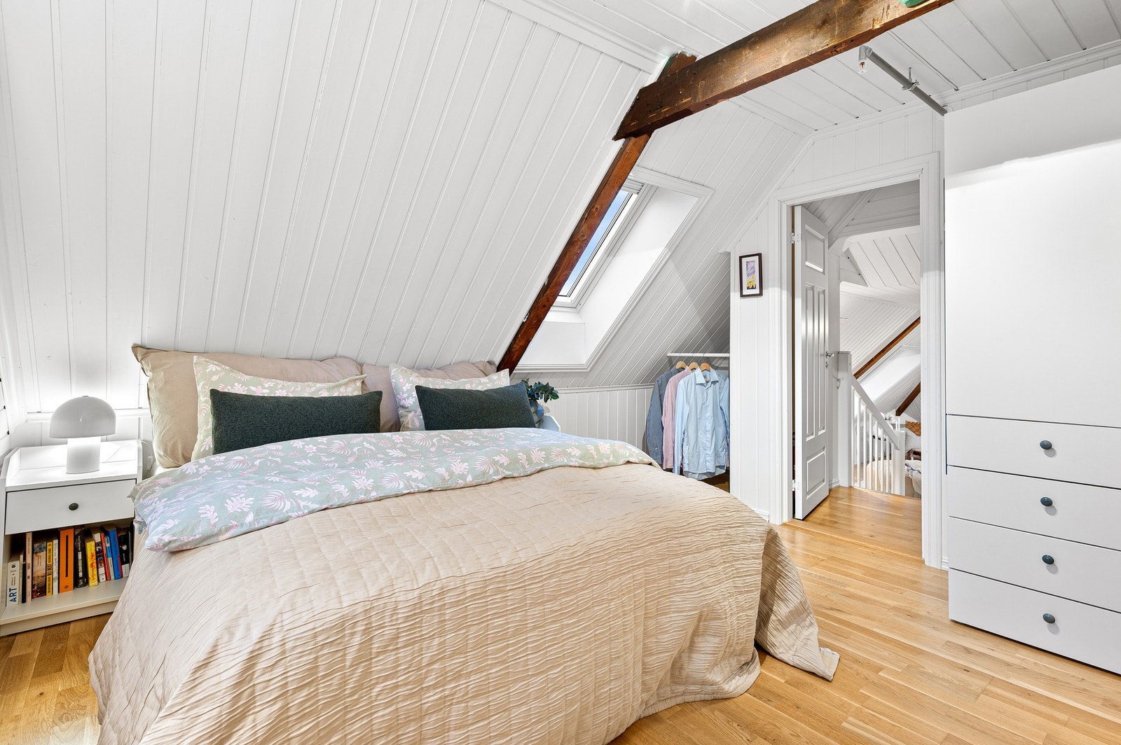 Romslig loftsoverom med skråtak, synlige bjelker og god plass til dobbeltseng og oppbevaringsmøbler. Galleribilde