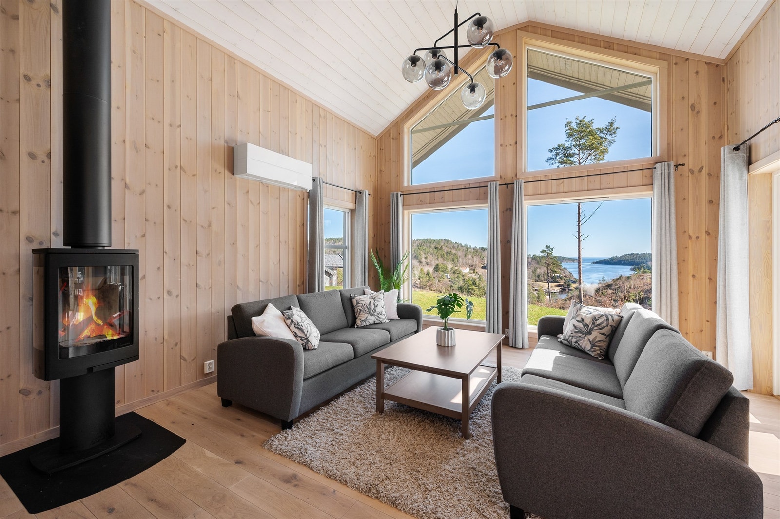 Stue med åpen himling som gir en luftig og god romfølelse. Store vinduer som gir rikelig med lys, slipper naturen inn og skaper en nærhet til omgivelsene. Galleribilde