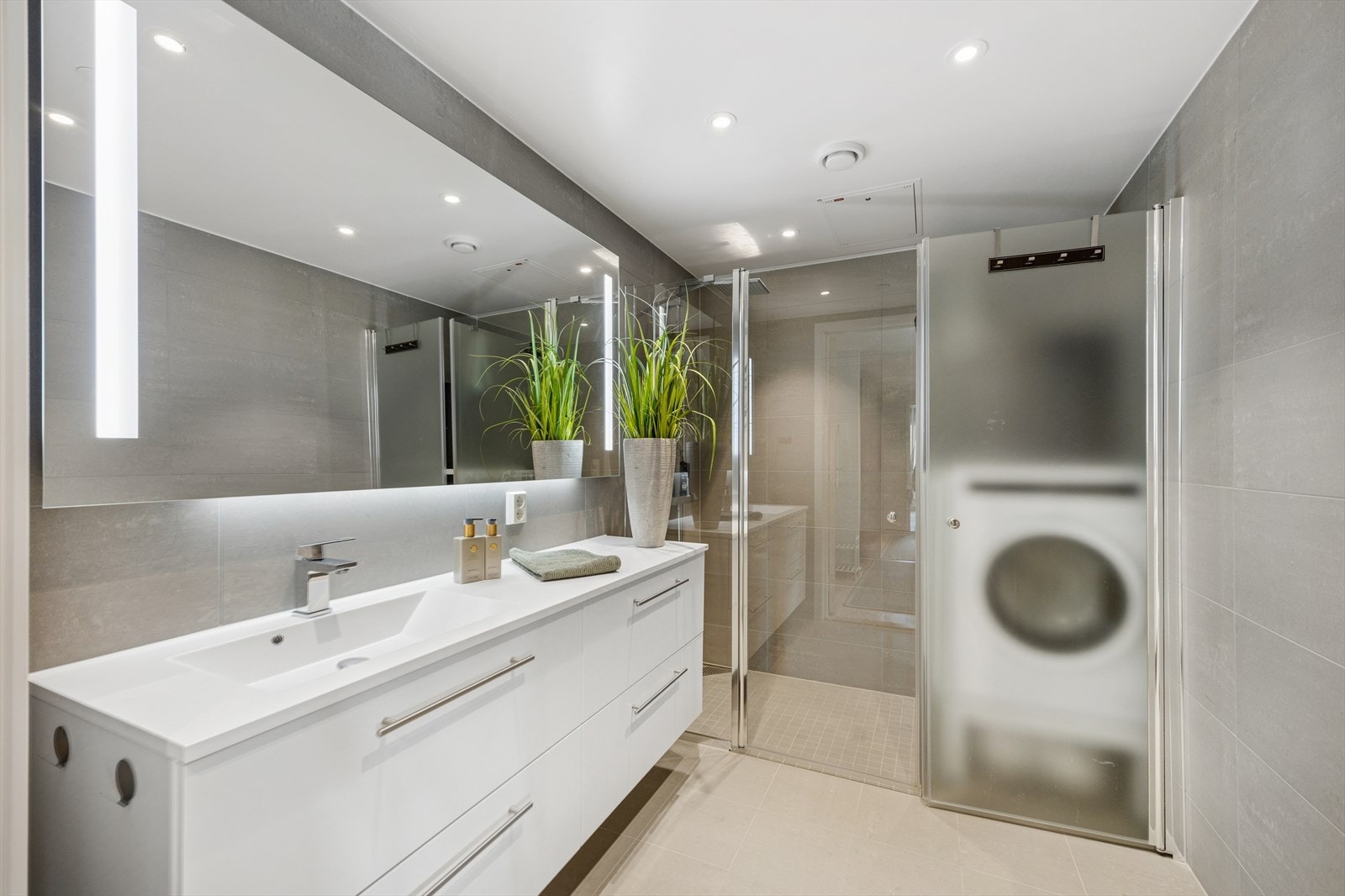 Moderne og flislagt baderom fra byggeår, 2023 og har elektriske varmekabler i gulv. Veggene har fliser og taket er malt. Badet er utstyrt med innredning med nedfelt servant, veggmontert toalett, dusjvegger/hjørne og opplegg for vaskemaskin. Galleribilde