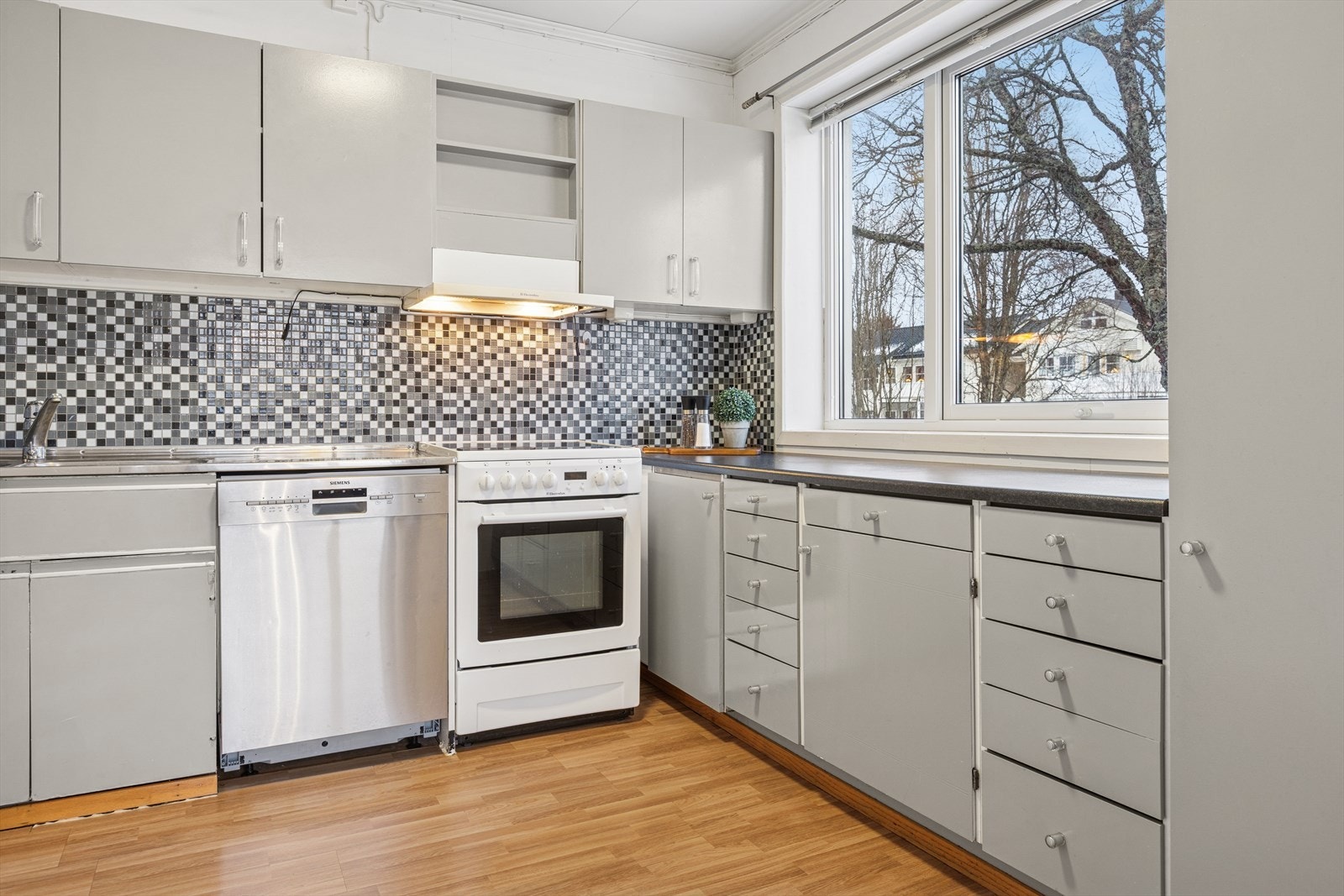 Over benken finner du fliser kombinert med baderomspanel, som gir en enkel og funksjonell overflate. Rommet er utstyrt med kjøkkenventilator med avtrekk til fri luft, noe som sikrer god luftkvalitet under matlaging. Galleribilde