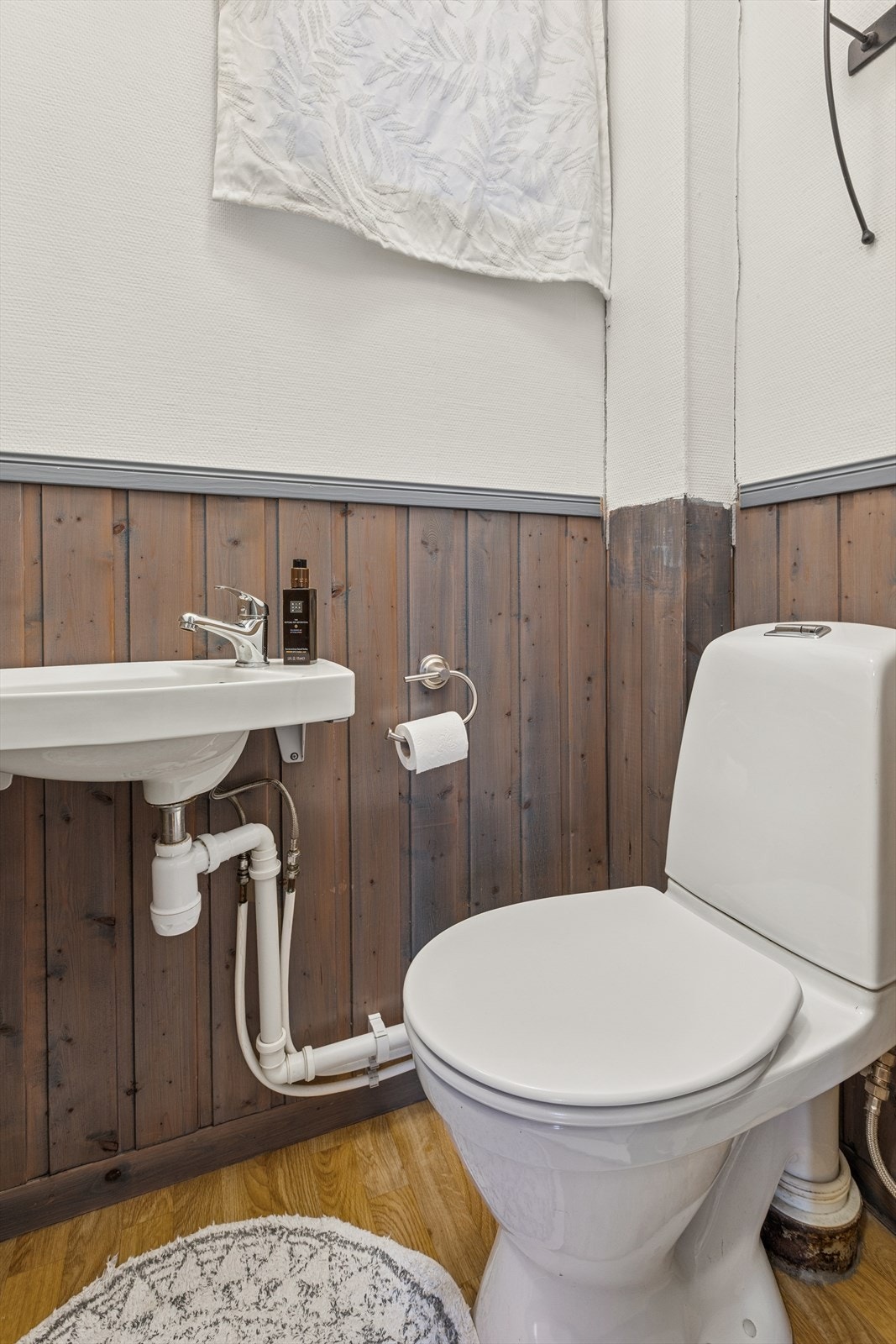 Toalettrommet i 1. etasje har belegg på gulv, vegger med malt panel og tapet, samt gulvstående toalett og vegghengt servant. Naturlig ventilasjon gir god luftgjennomstrømning. Et enkelt, men praktisk rom med gode muligheter for modernisering. Galleribilde