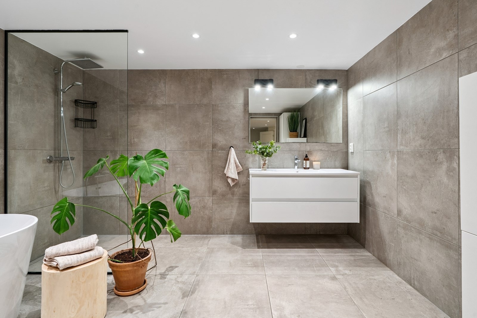 Badet har moderne innredning med glatte fronter, stort speil over servanten, praktisk skuffeseksjon og et ekstra seksjon for god oppbevaringsplass Galleribilde