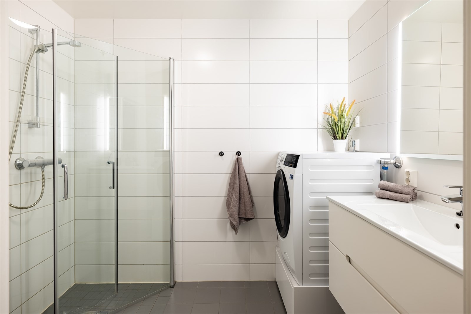 Lyst flislagt bad som består av servant, innfellbare dusjdører, wc og opplegg for vaskemaskin. Galleribilde