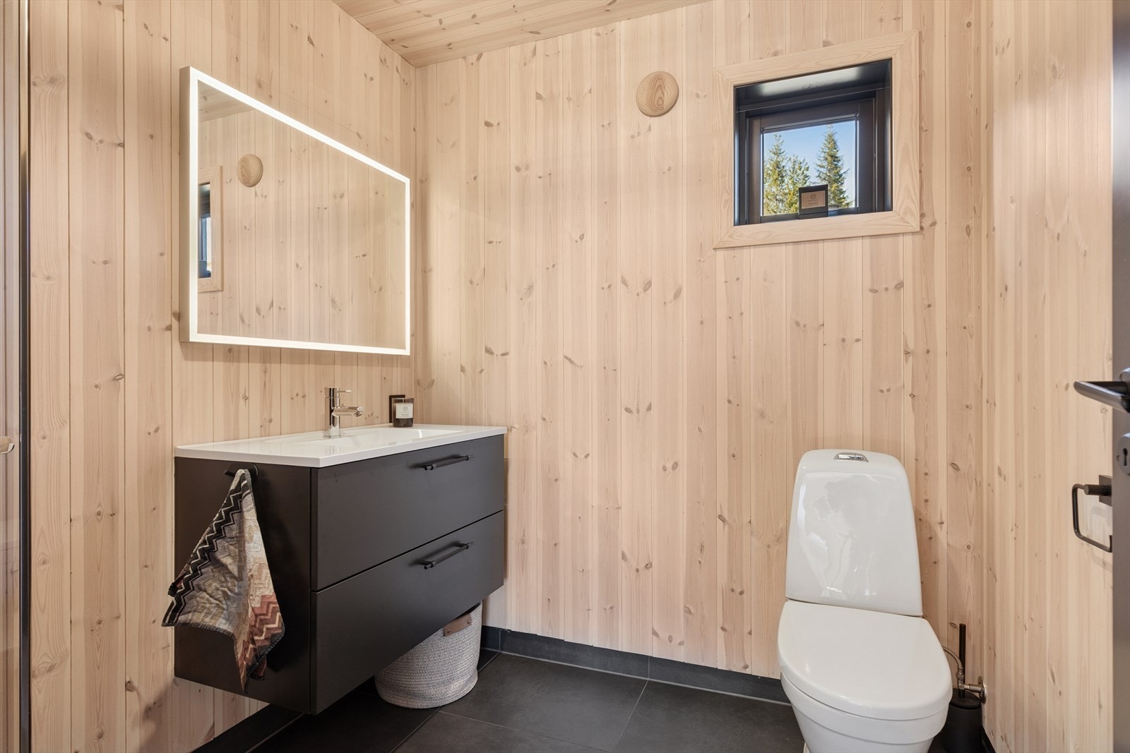 Badet i 1. etasje har et mørkt flislagt gulv og pene vegger med panel samt flis i dusjsone. Galleribilde