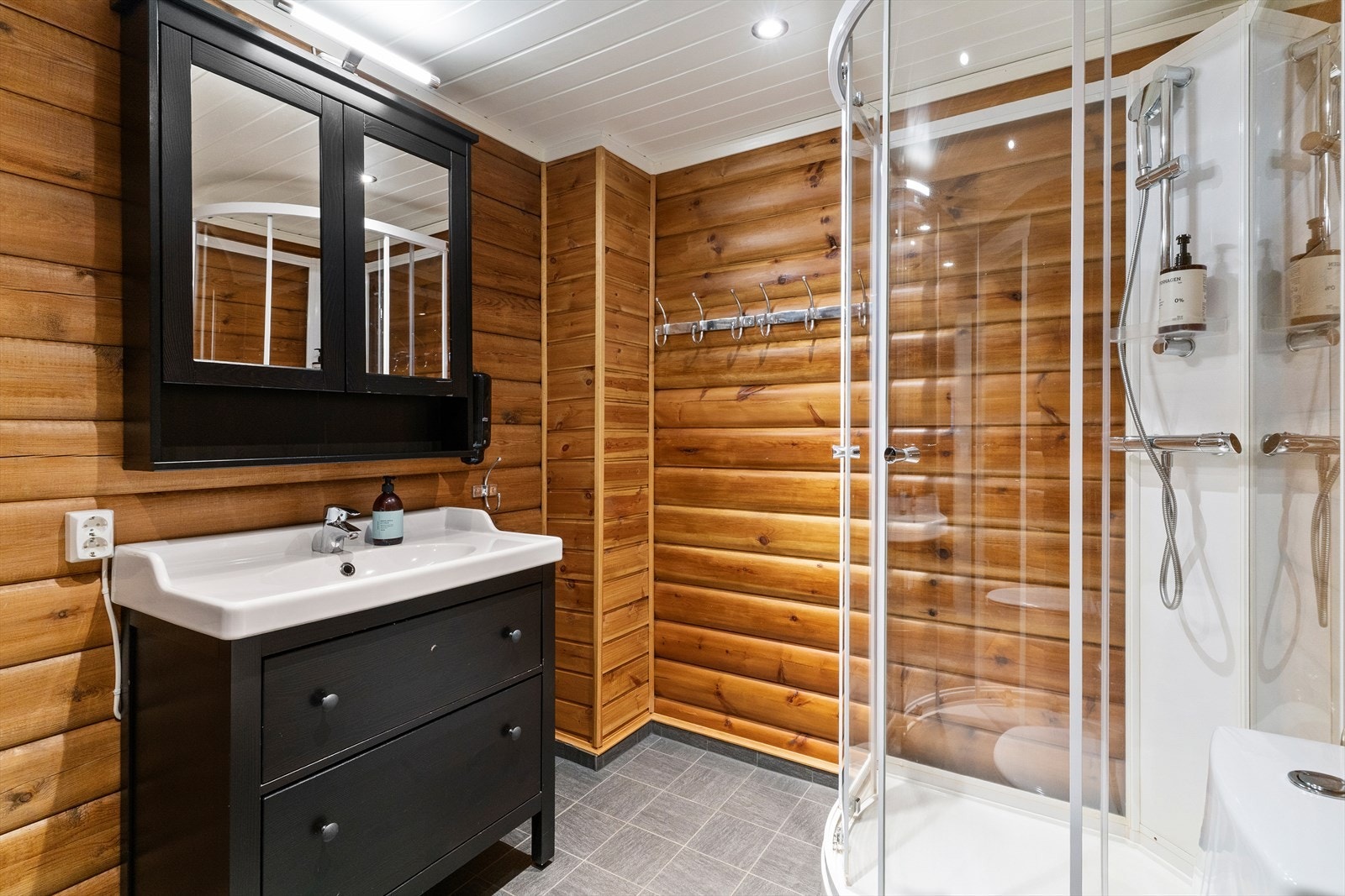 Badet inneholder lukket dusjkabinett, behandlet innredning med servanttopp, montert toalett, speil på vegg over servant og opplegg for vaskemaskin. Galleribilde