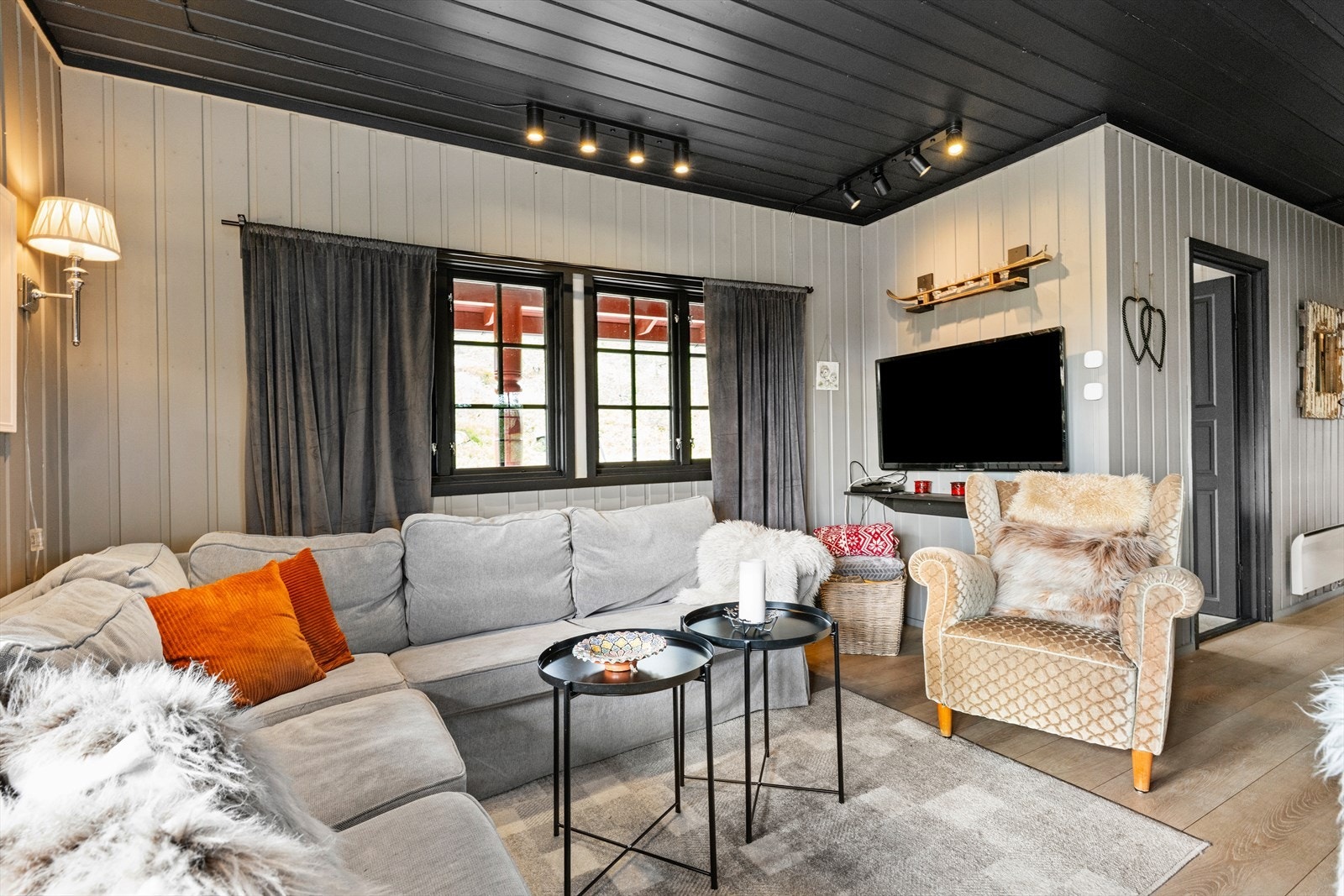 Hytta har en hyggelig sofakrok med bord og tv på vegg, åpen løsning mot spisestuen. Delikate fargevalg, og tidsriktig innredning med belysning og gardiner i en lun fargepalett. Galleribilde