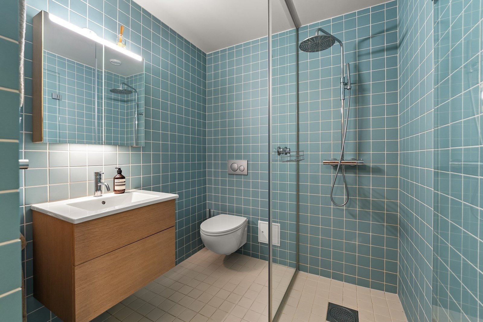 Lekkert bad med servant med skap og tilhørende speilskap, vegghengt toalett og dusj med glassvegg. Galleribilde