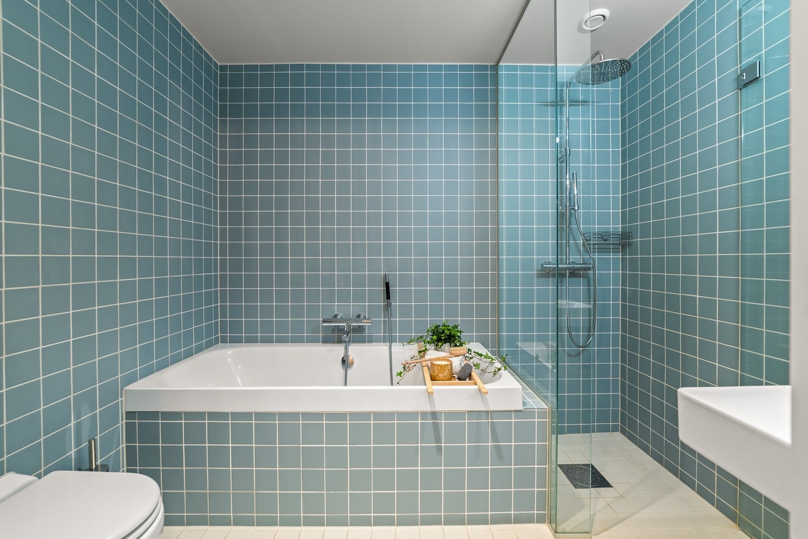 Romslig bad med badekar, dusj, vegghengt toalett og porselensservant med hylleløsninger av eikeplater Galleribilde