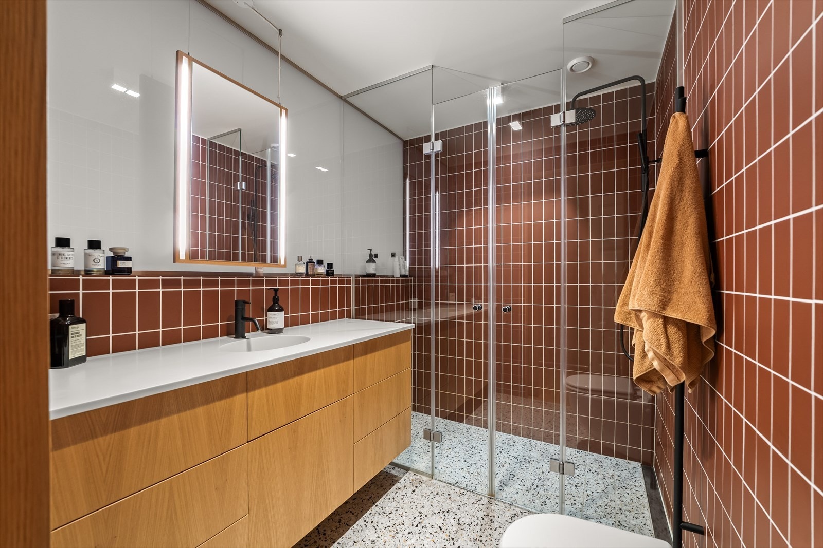 Badet er innredet med heldekkende Corian servantbenk med integrert servant samt underliggende servantskap, veggklosett og dusj. Galleribilde