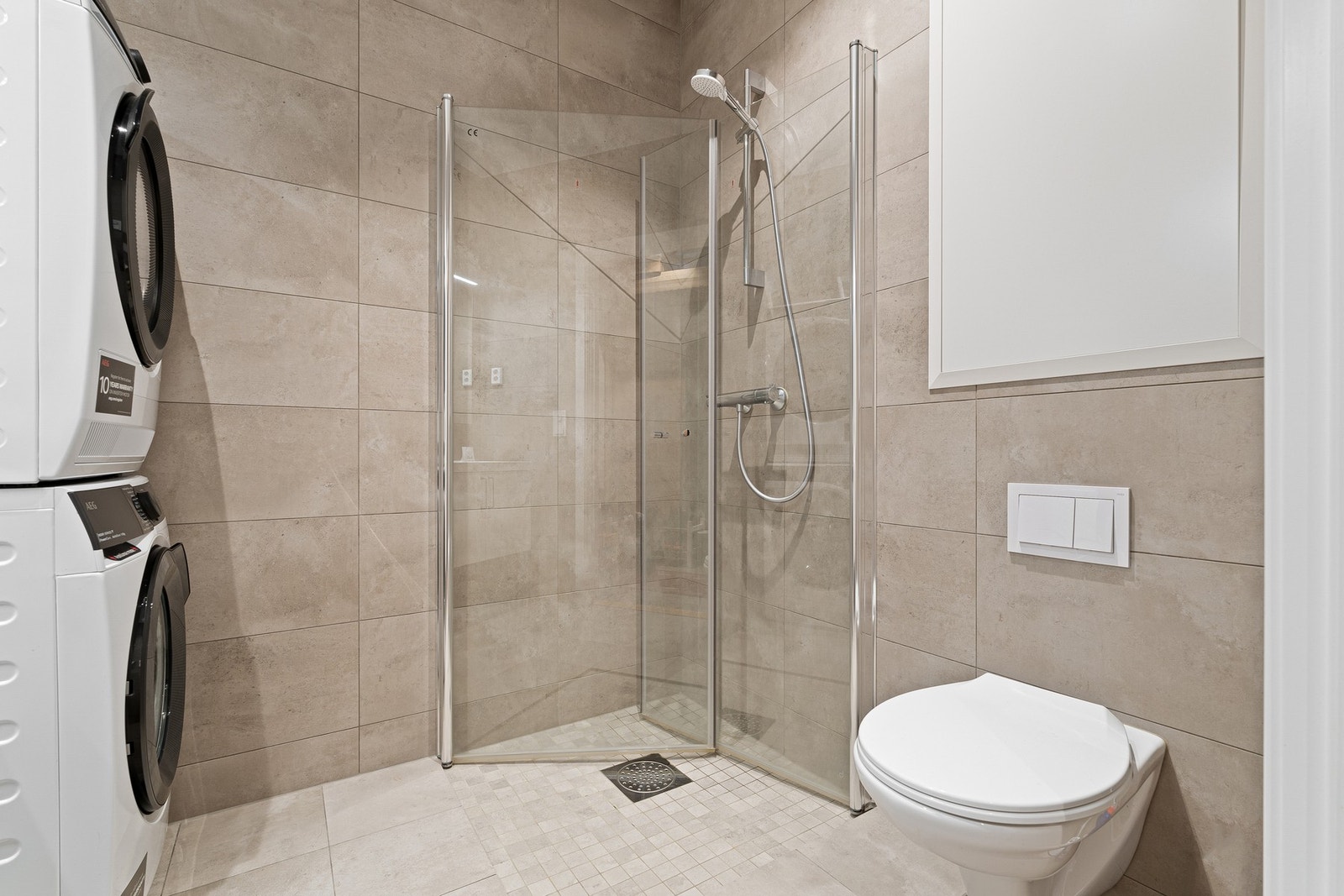 Badet er utstyrt med dusjhjørne med innfellbare dusjdører og veggmontert toalett med skjult sisterne. Galleribilde