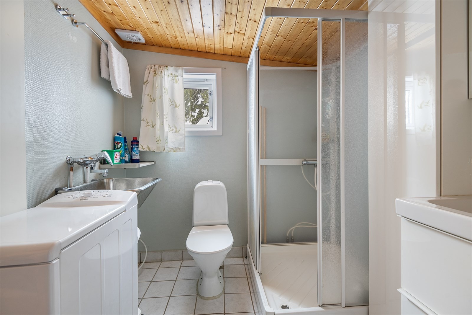 Baderom med malt tapet på vegg, panel i himling og lyse fliser på gulv. Galleribilde