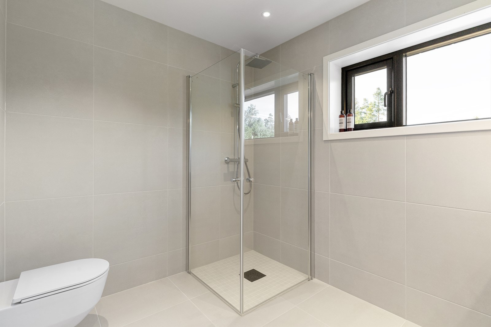 Også dette badet er utstyrt med vegghengt toalett og dusjnisje med glassvegger, samt nedfelt sone med mosiakkflis og lokalt fall til sluk. Galleribilde