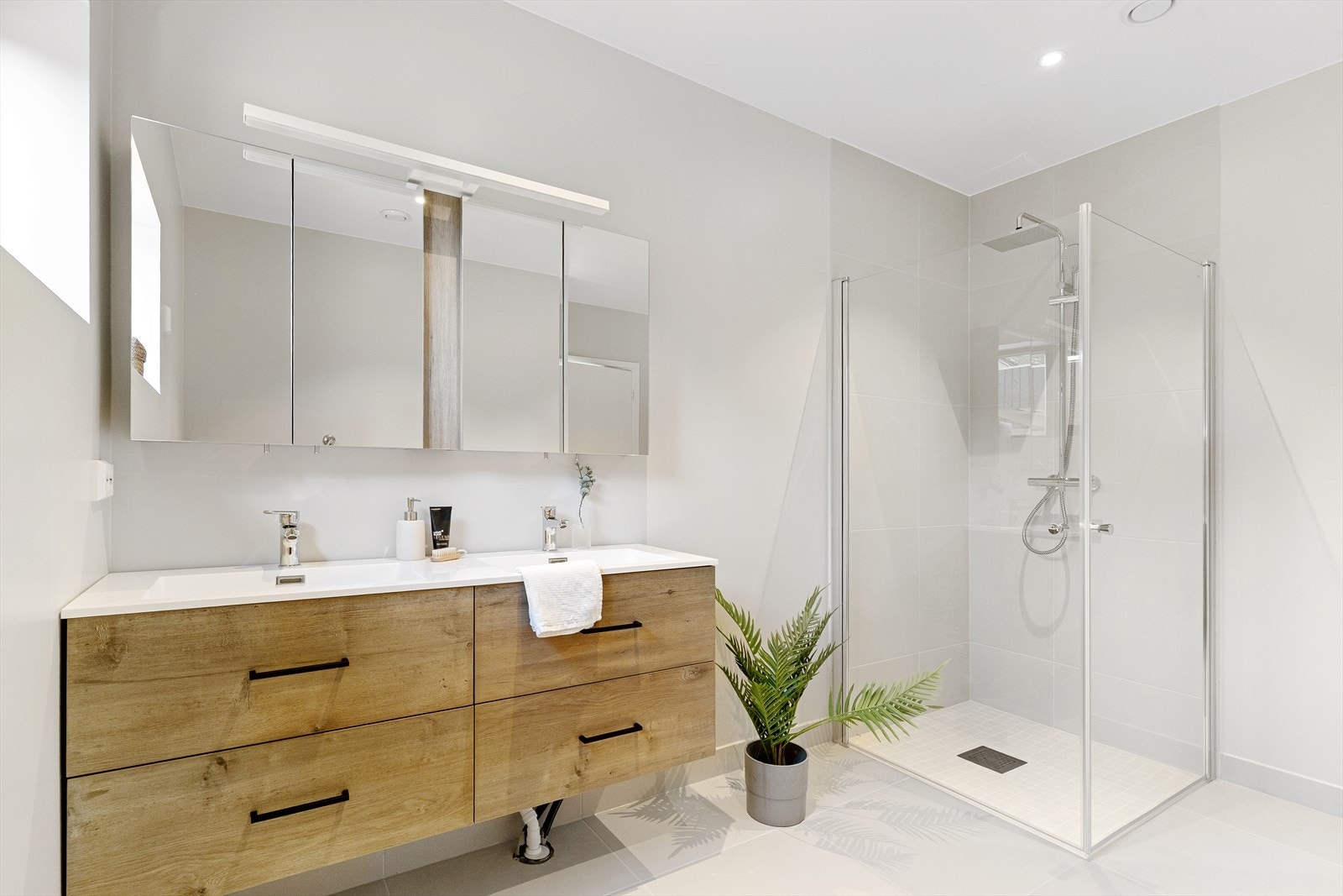 Badet er lekkert og romslig. Veggene er slette, for utenom dusjen som er belagt med flis. Regndusj, nedsenket nisje, og mosaikkflis for lokalt fall til sluket. Heldekkende dobbeltservant med skuffinnredning, skapspeil og belysning over. Galleribilde