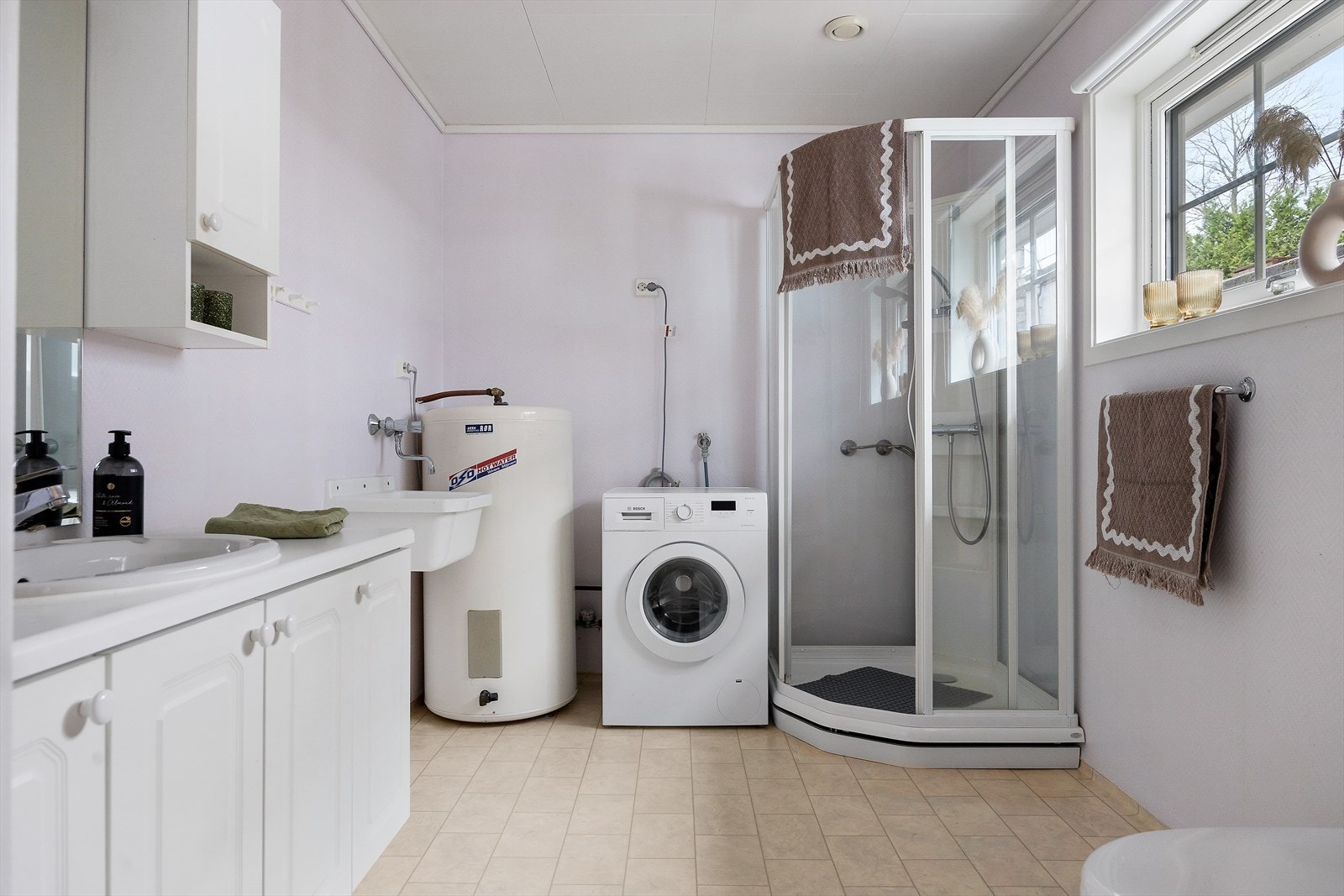 Bad/vaskerom er innredet med dusjkabinett, servant med benkeskap, toalett, speil samt opplegg for vaskemaskin og kondenstørketrommel. Det er også en praktisk utslagsvask av plast med armatur. Galleribilde