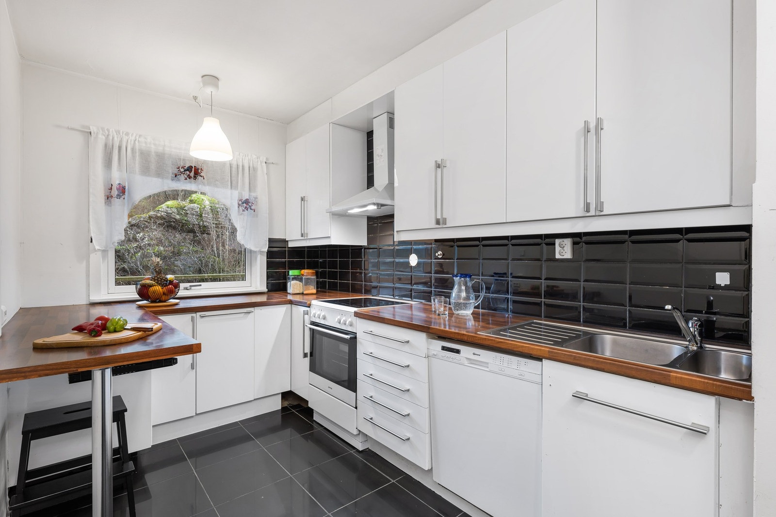 Romslig og lyst kjøkken, med slette fronter og laminat benkeplate med stål oppvaskkum. Galleribilde