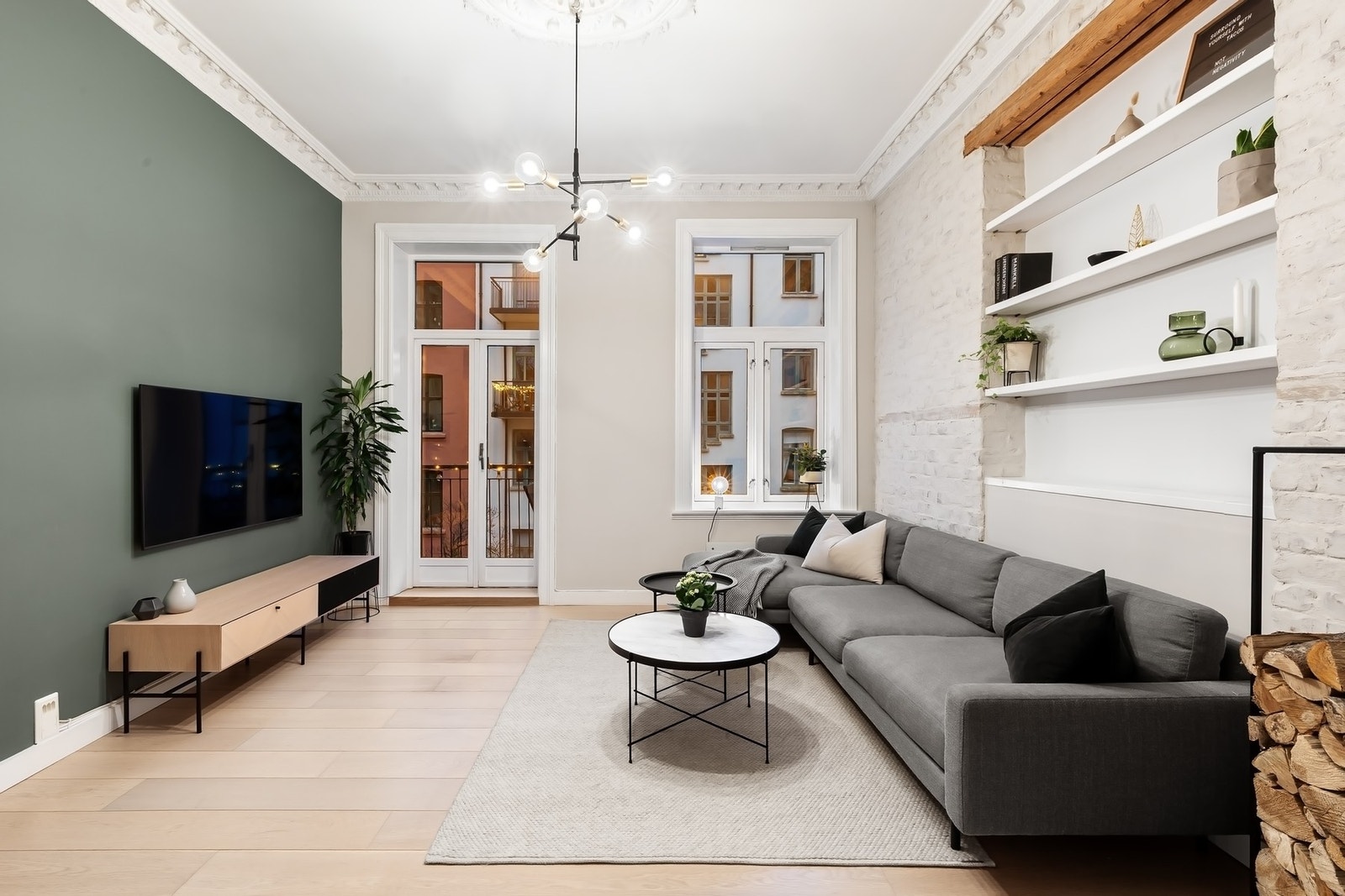 Teglsteinsvegg i kombinasjon med hylleløsning og orignal takbjelke som gir et eget særpreg i stuen Galleribilde