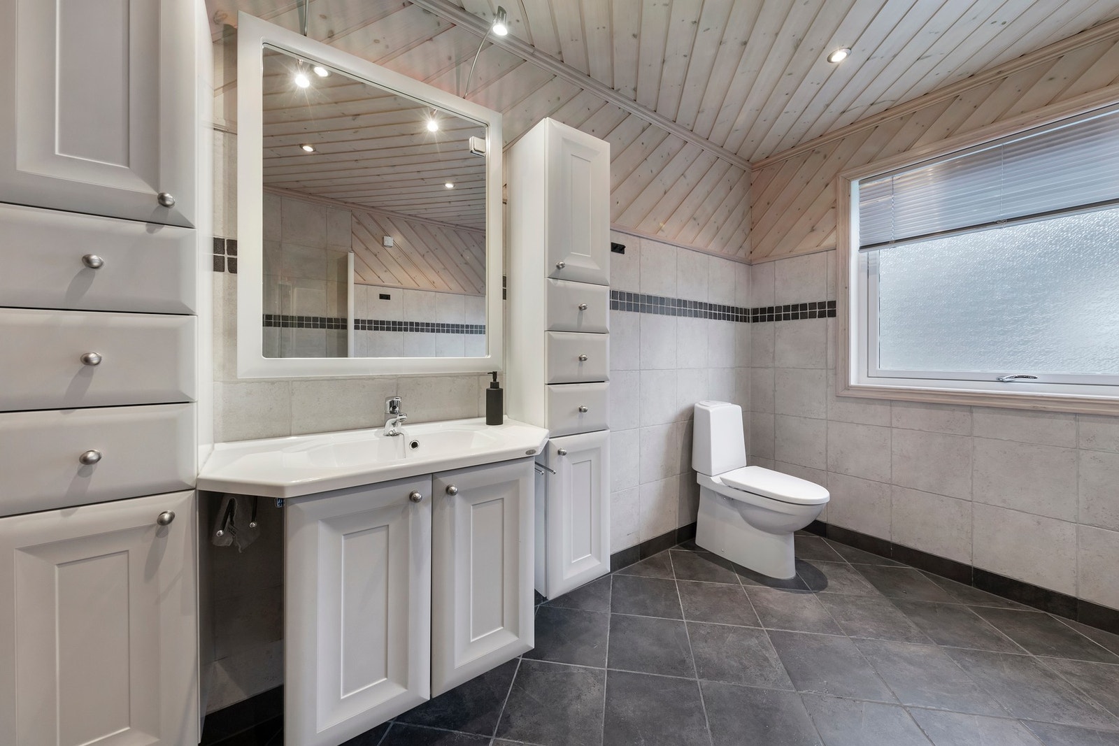 Bad i hovedetasje har flislagt gulv med elektriske varmekabler og foliert innredning med heldekkende servant. Dusjhjørne i glass, badekar og gulvmontert toalett Galleribilde