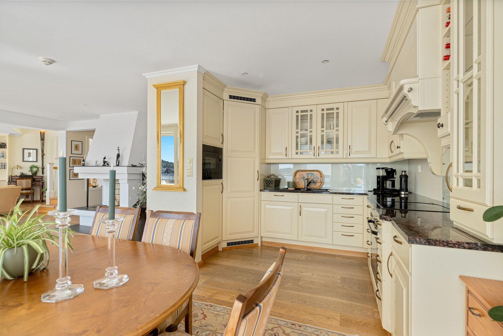 Tradisjonell kjøkkeninnredning med takhøye skap og benkeplate av stein. Integrerte hvitevarer og kjølehjørne. Galleribilde