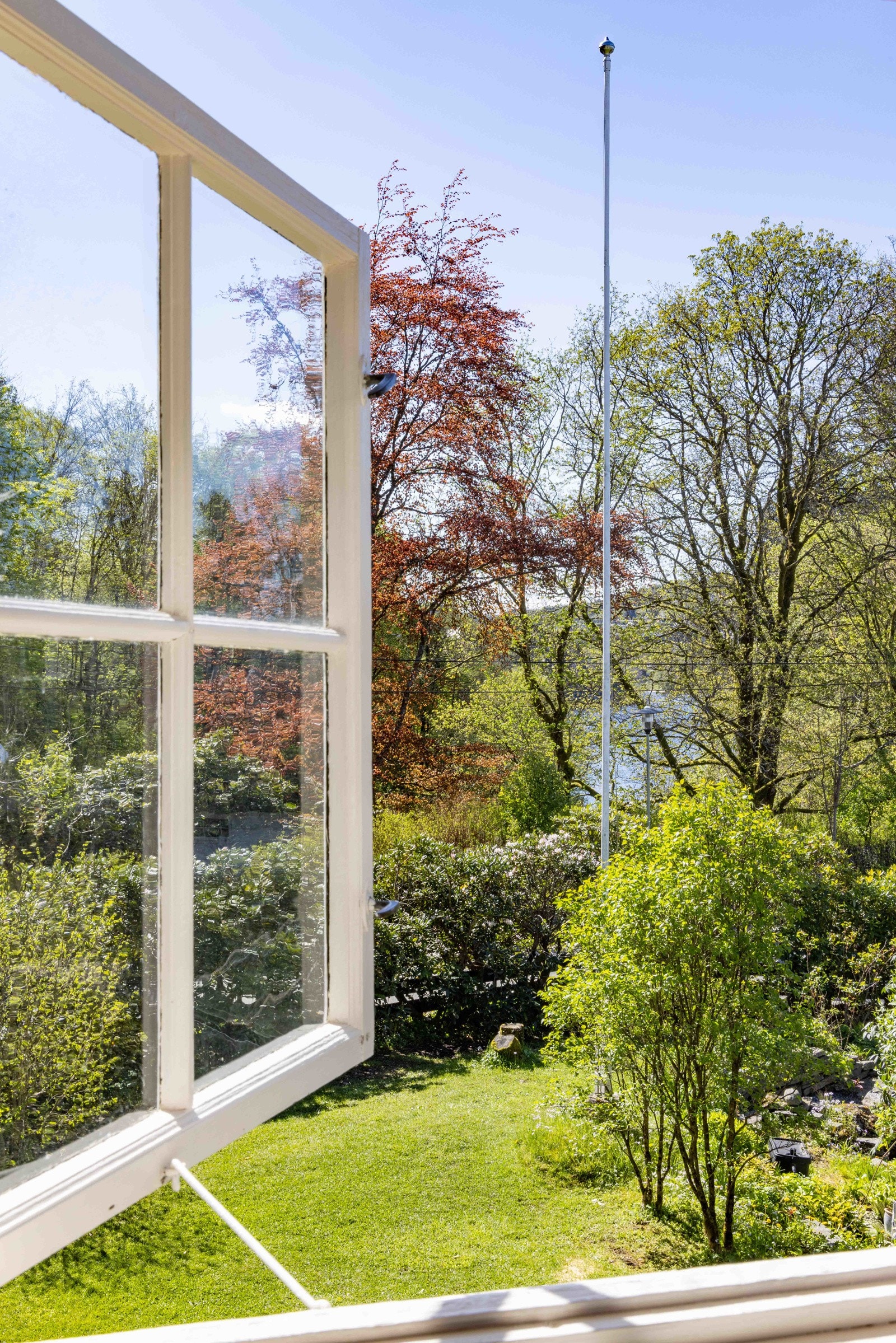 Utsikt fra soveromsvinduet mot hagen og man kan skimte Nordåsen bak trærne. Galleribilde