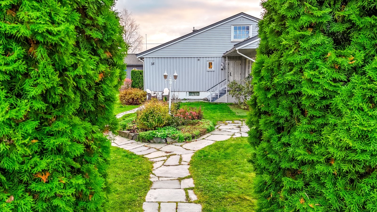Inngangspartiet er omkranset av grønn beplantning og har en steinlagt gangvei. Galleribilde