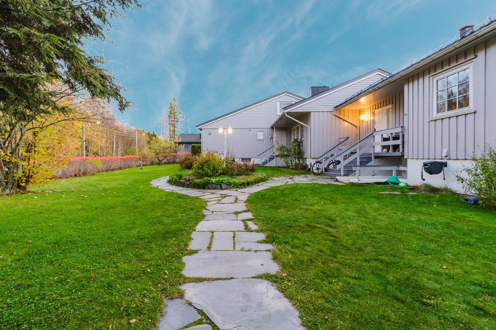 Steinlagt gangvei fører til boligens inngang, omgitt av frodige busker og plen. Galleribilde