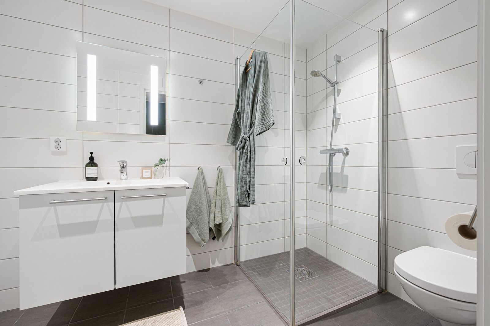 Pent og funksjonelt bad med flislagte overflater og dusjhjørne med glassvegger. Galleribilde