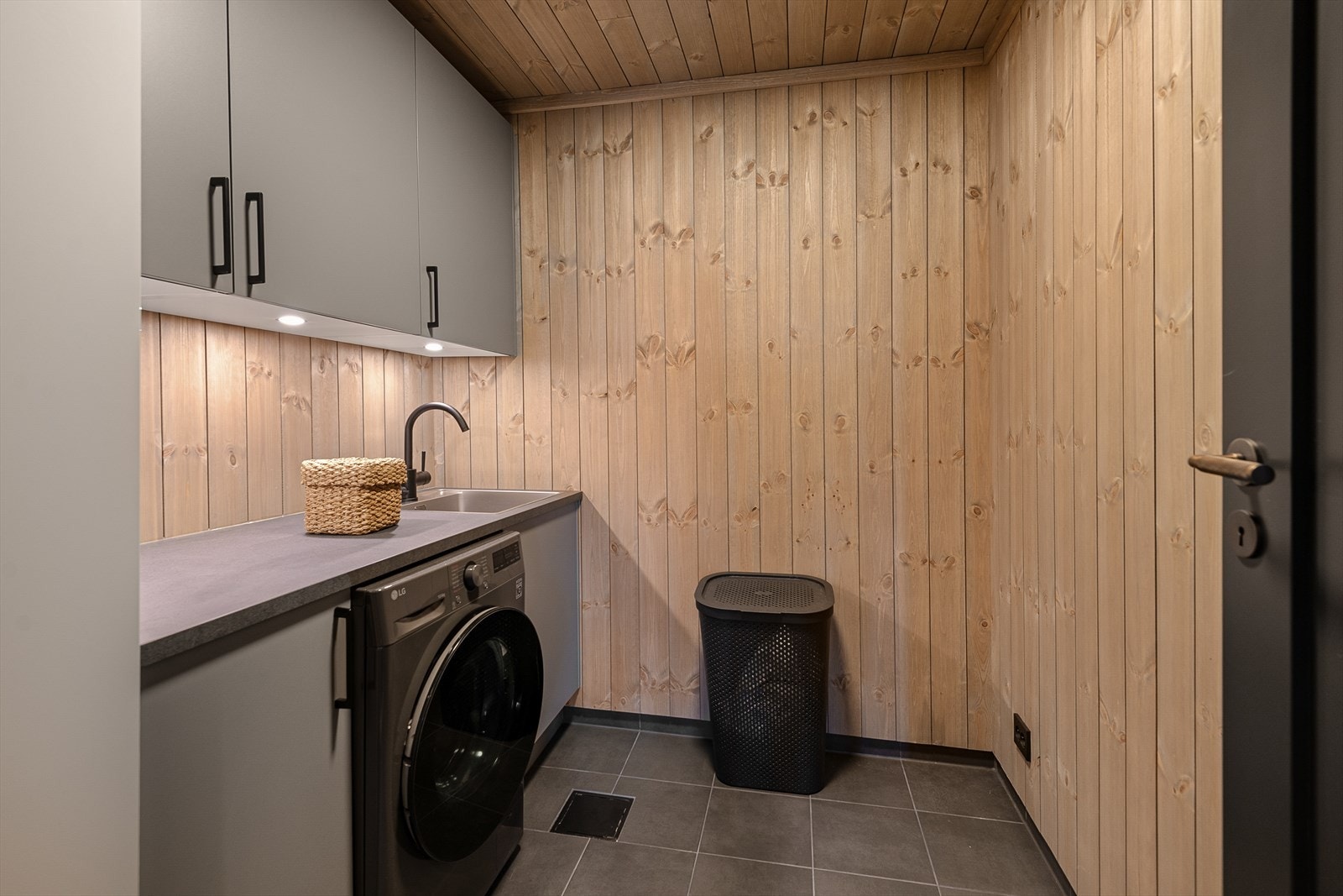 Hytten byr på et praktisk vaskerom, som er beliggende i underetasjen. Overflatene er med fliser på gulv og panel på vegger. Videre er rommet utstyrt med servant med underskap, tørkeskap og det er opplegg for vaskemaskin her. Det er gulvvarme i gulvet. Galleribilde