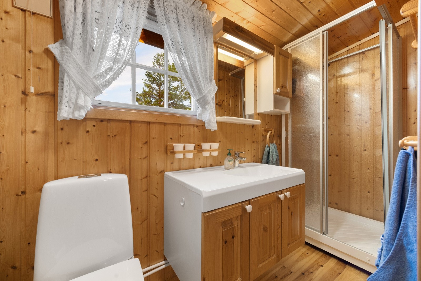 Badet har tregulv, trepanel på vegger og i himling. Badet har gulvmontert toalett, servant med innredning og dusjkabinett. Rommet ventileres via naturlig avtrekk. Galleribilde