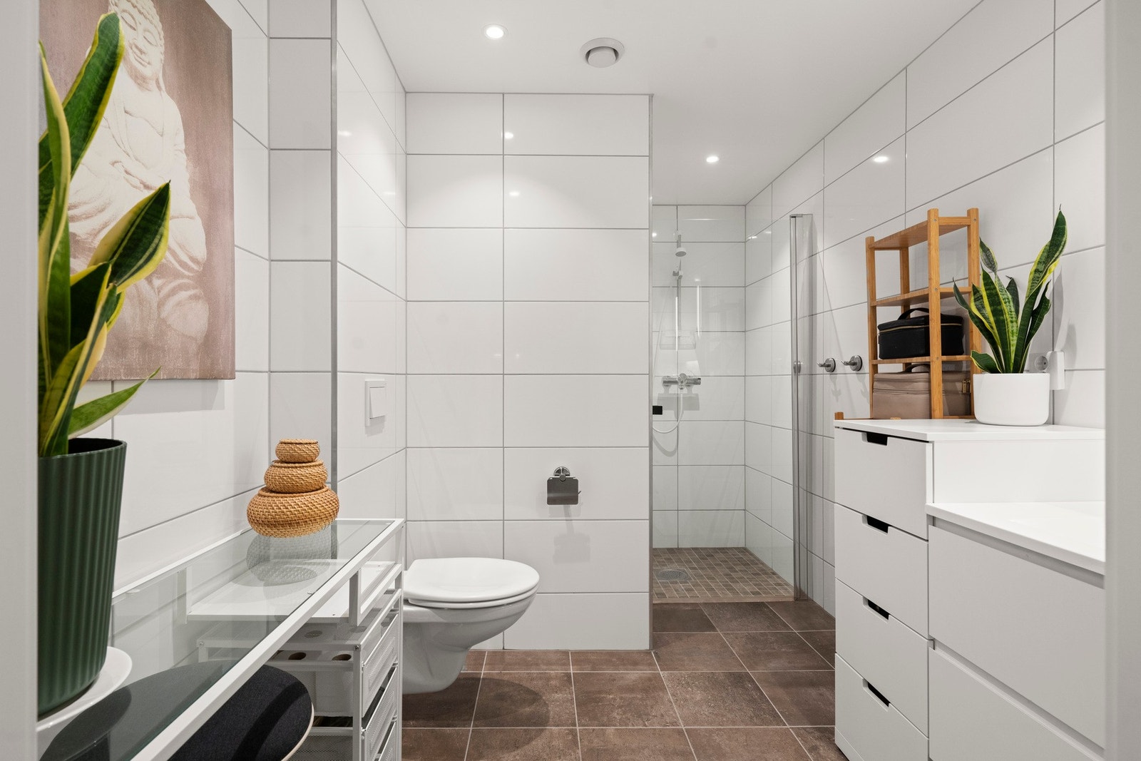 Lekkert bad med fliser på både gulv og vegger, samt malt himling. Rommet er utstyrt med veggmontert toalett, servant med innredning og speil, samt en praktisk dusjnisje med glassdører. Gulvet har elektriske varmekabler og dokumentert banemembran med plast Galleribilde