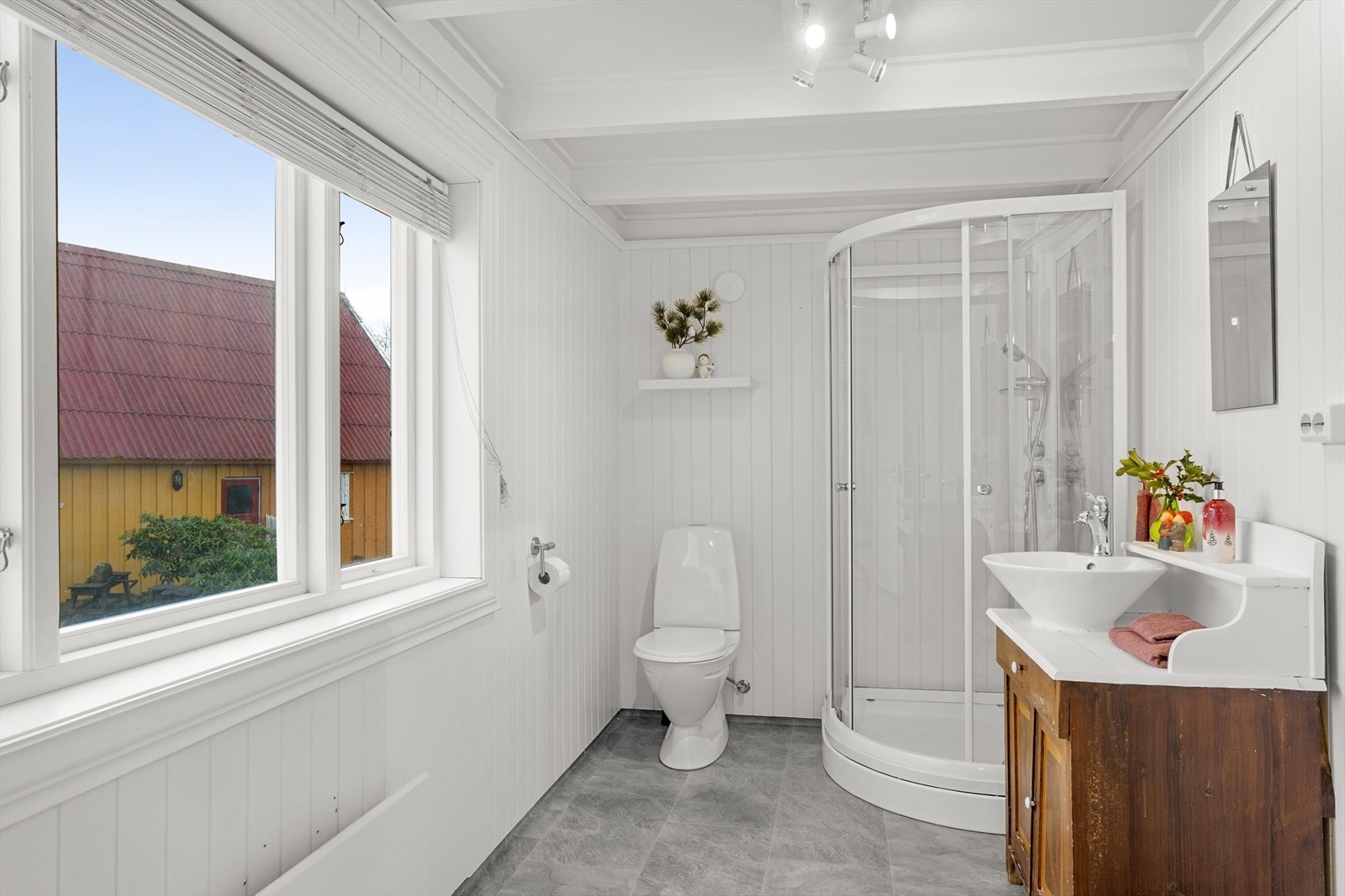 Baderommet er er utstyrt med panelovn, dusjkabinett, gulvstående toalett, frittstående servant montert i eldre, ombygd kommode samt opplegg for vaskemaskin. Galleribilde