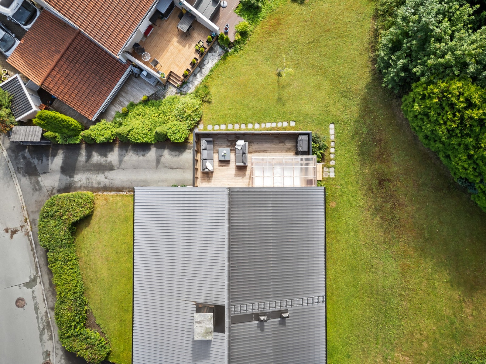 I sommer tok selgerne bilder av uteområdet for å vise hvordan det fremstår i den beste årstiden. Tomten er meget pent opparbeidet med en frodig og skjermet hage som strekker seg rundt boligen. Galleribilde