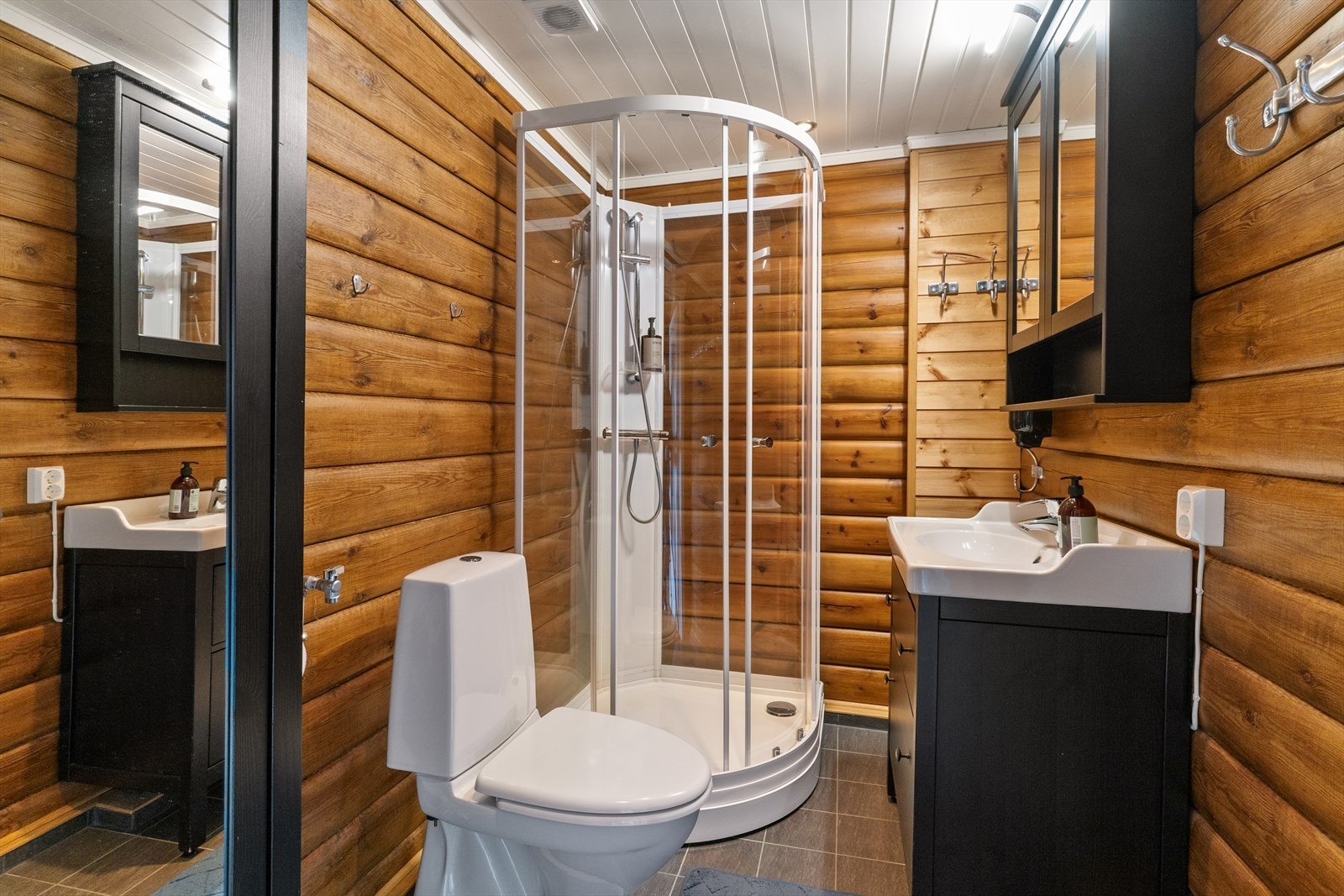 Badet inneholder behandlet innredning med servanttopp hvor det er montert skap på vegg over servant med speil på dører, toalett, dusjkabinett og opplegg for vaskemaskin. Galleribilde