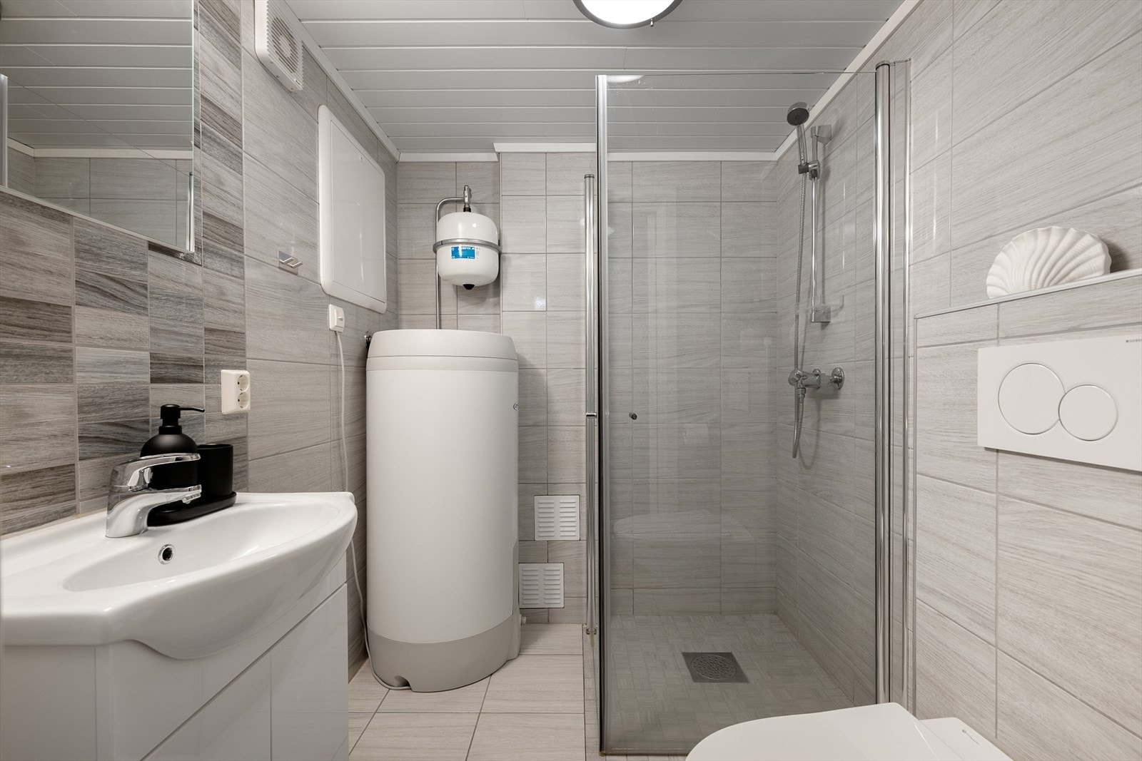 Kjellerbadet er stilfullt innredet med lyse, delikate fliser, dusj og vegghengt toalett Galleribilde