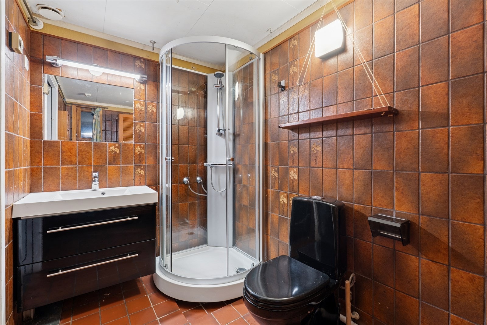 Eldre flislagt bad utstyrt med dusjkabinett, gulvstående toalett og moderne baderomsinnredning. Galleribilde