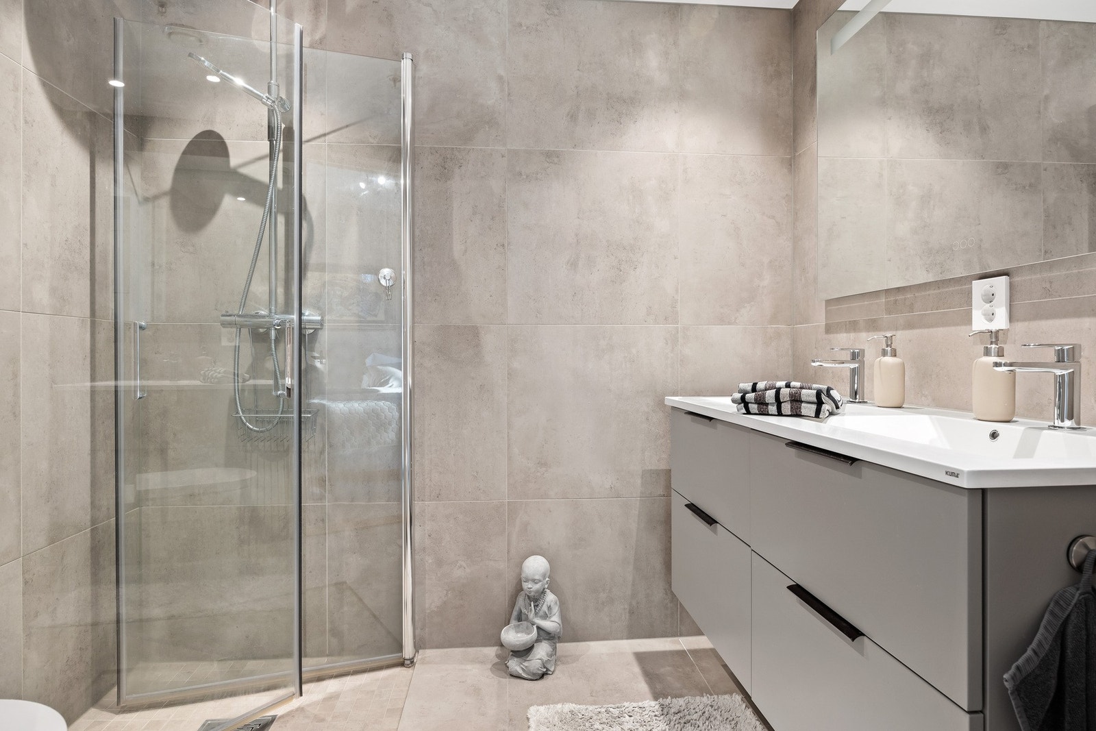 Lyst, flislagt baderom innredet med dusjnisje, dobbel servant med skuffeseksjon og klosett. Galleribilde