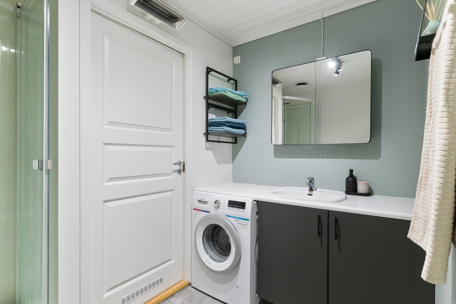 Badet inneholder innredning, benkeplate med vask, opplegg til vaskemaskin, dusjkabinett og toalett. Galleribilde