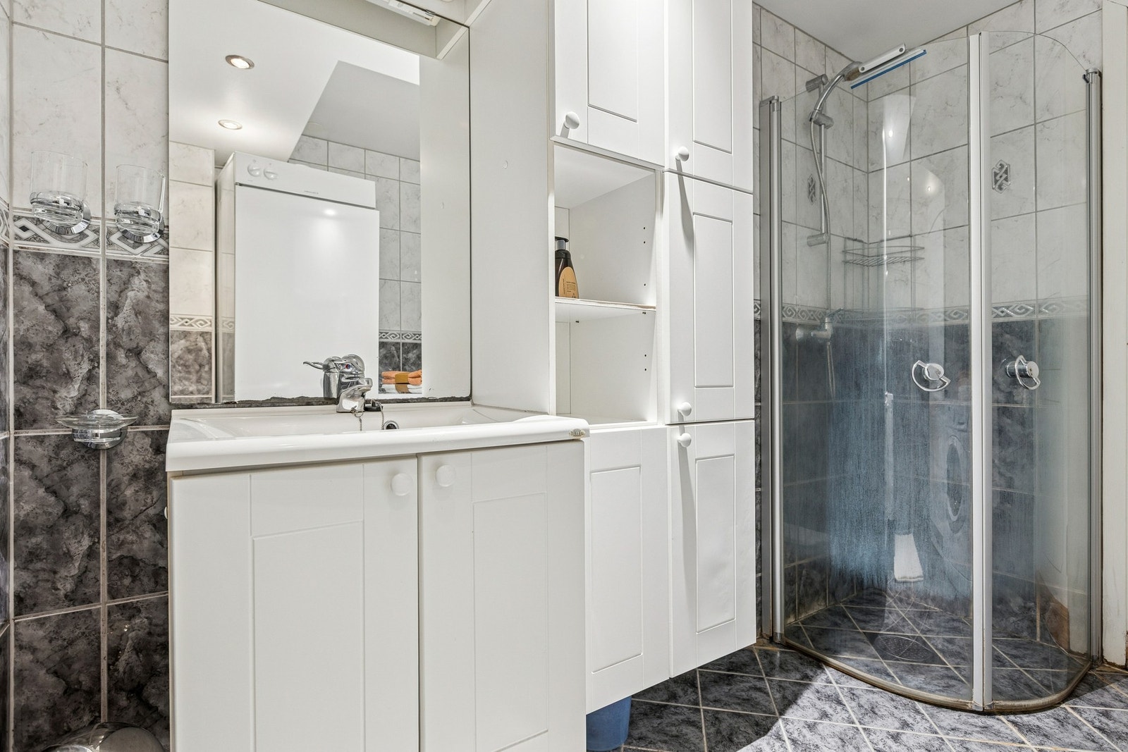 Badet er utstyrt med toalett, dusjhjørne i glass og servantinnredning med speil. Galleribilde